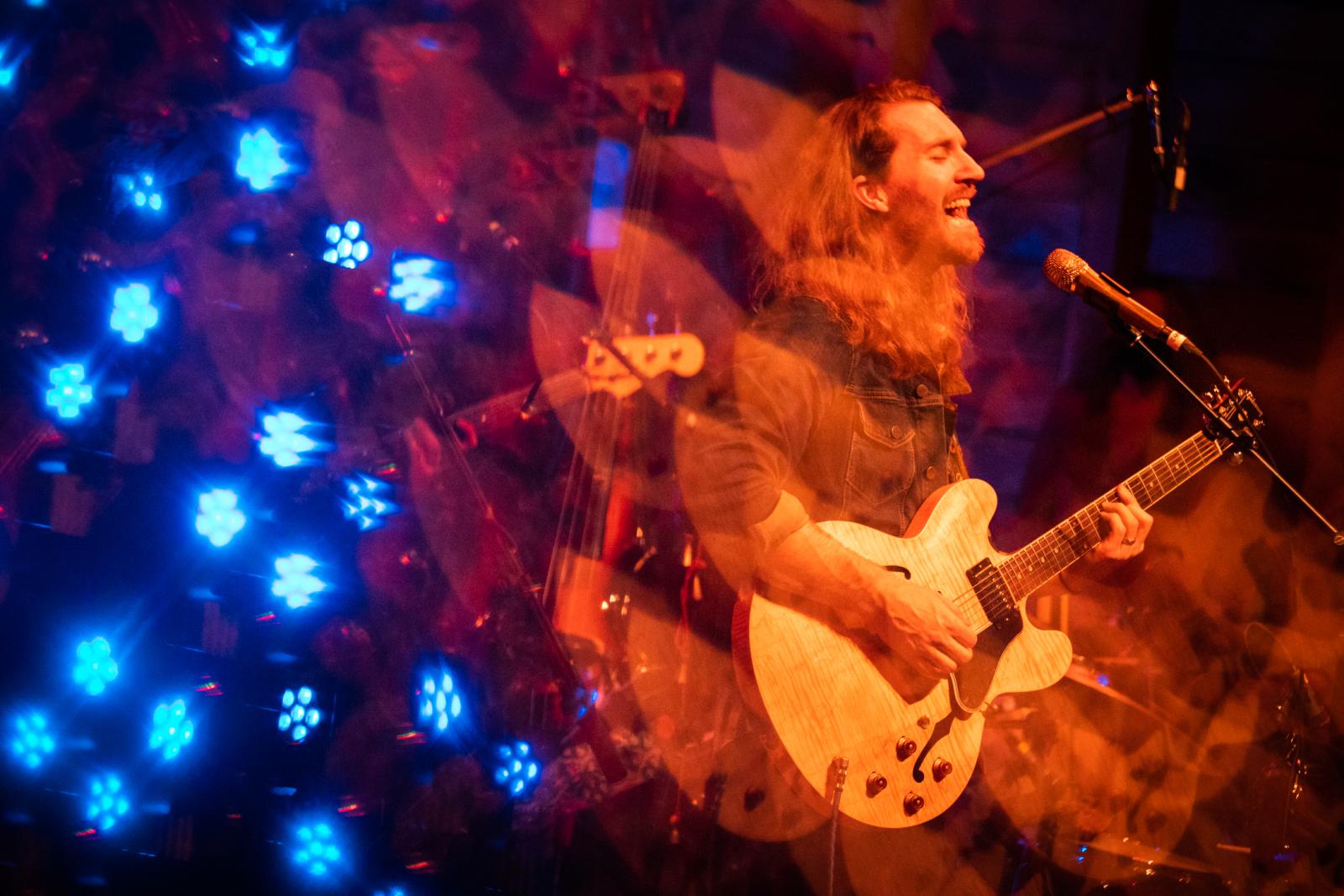 Image of Grahame Lesh with blurs of blue and orange from concert lights