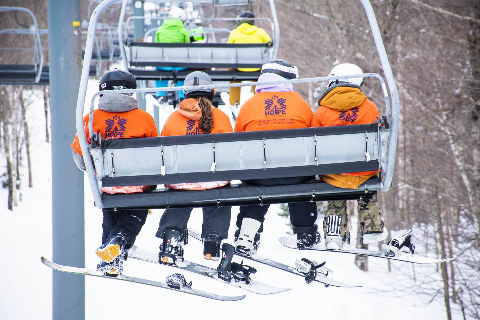 4 snowboarders in orange shirts on the lift