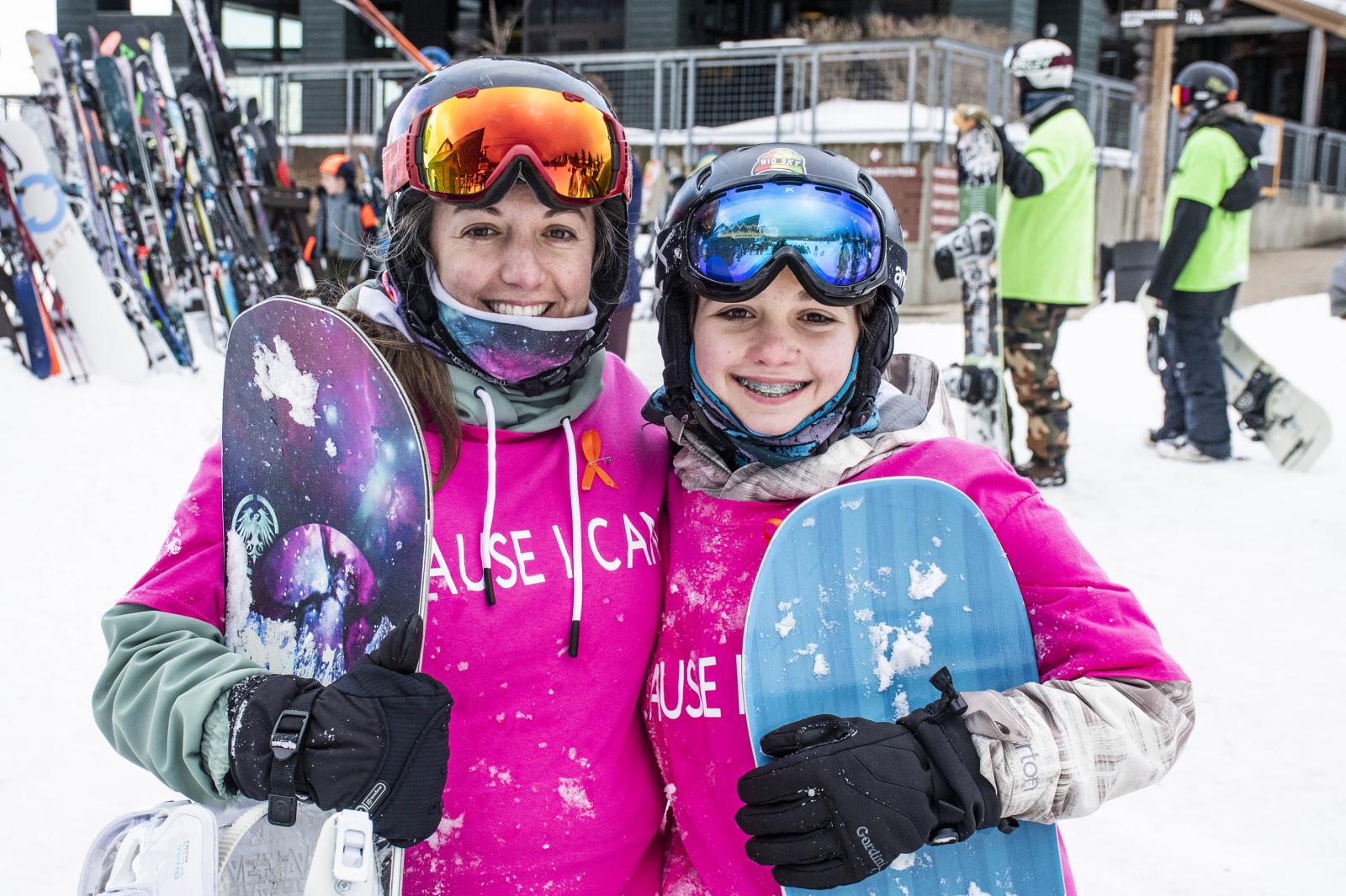 two snowboarder girls smiling in pink shirts 