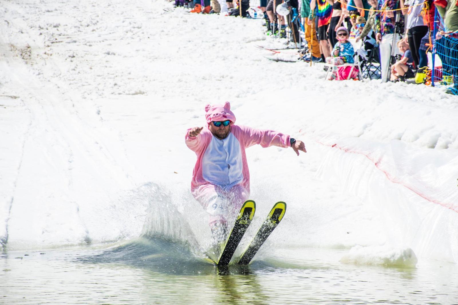 Skier in a pink costume gliding across a snowy slope, crowd watching.