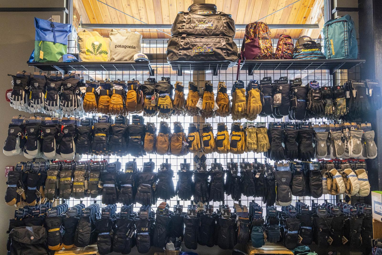 Wall display of colorful backpacks and rows of gloves in a well-lit store.