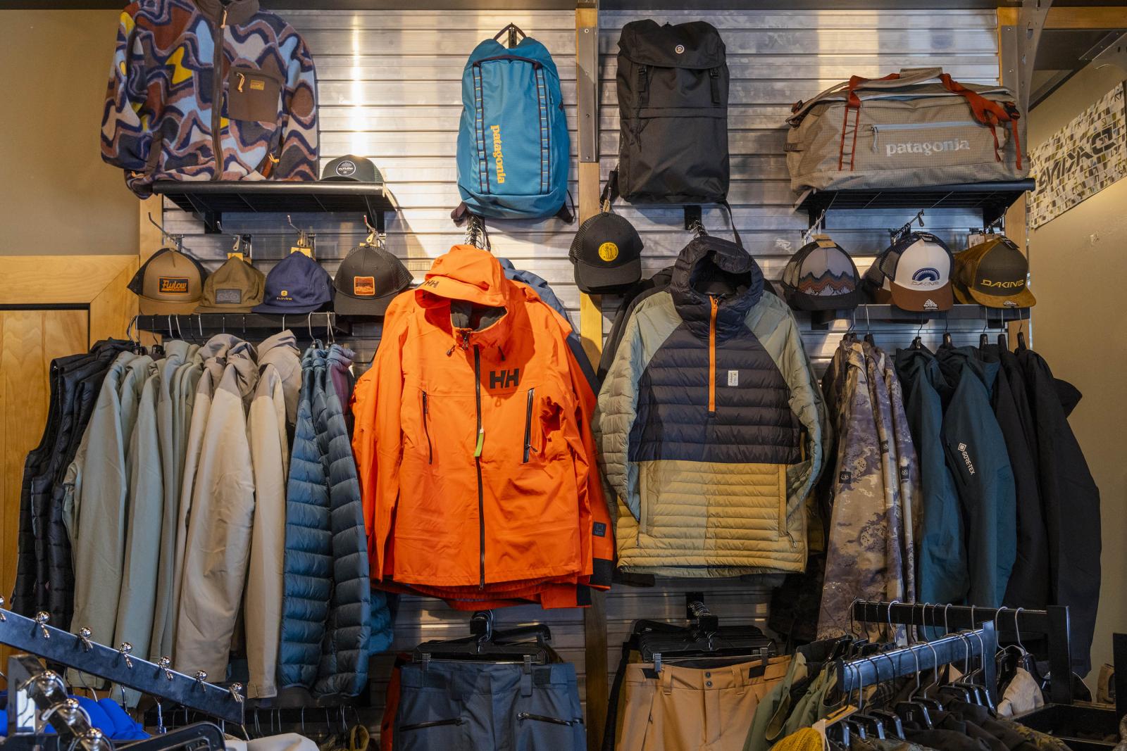 Outdoor apparel display with jackets, bags, and caps on shelves.