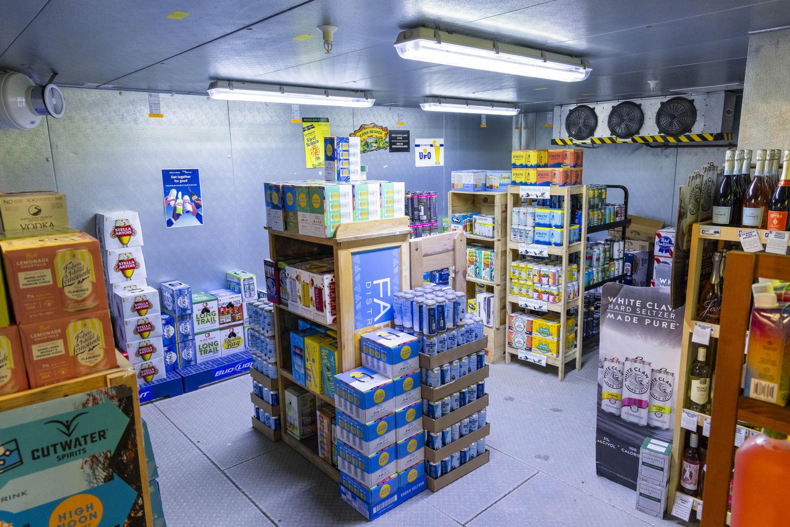 Storeroom with shelves stacked with colorful boxes and bottles, fluorescent lighting overhead.