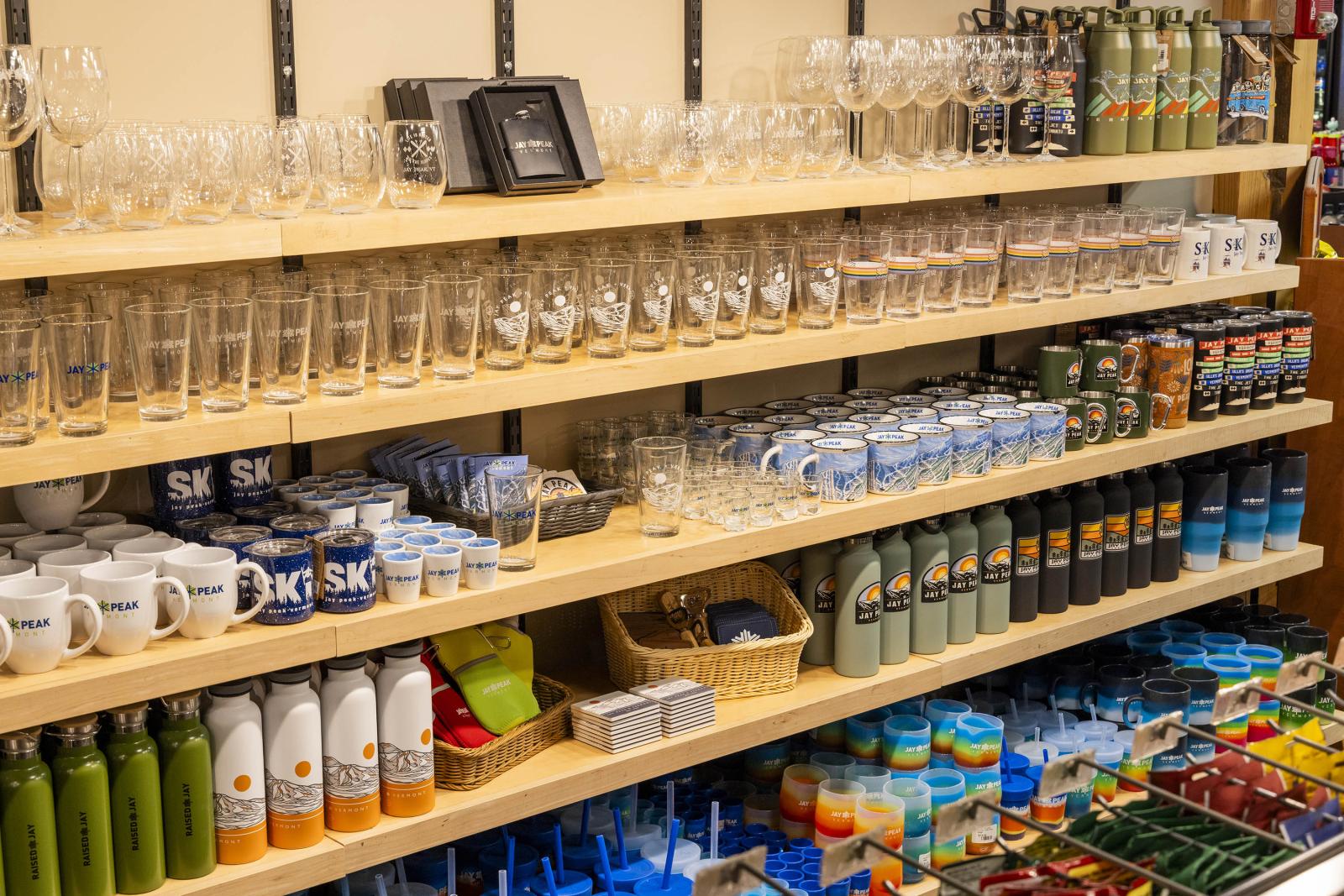 Shelves with glasses, mugs, bottles, and packaged items in a store setting.