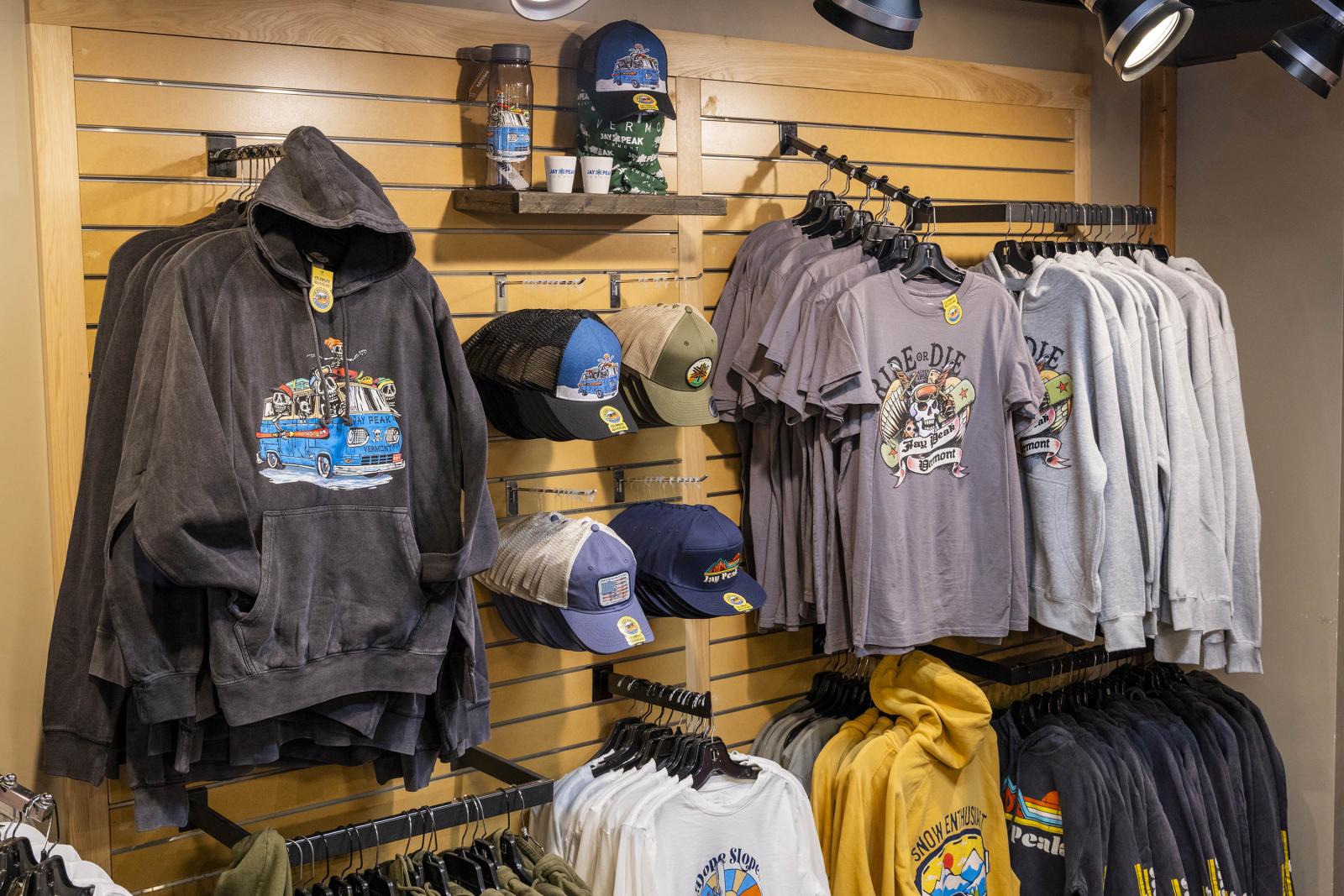 Clothing display with hoodies, caps, and t-shirts on wooden wall racks.