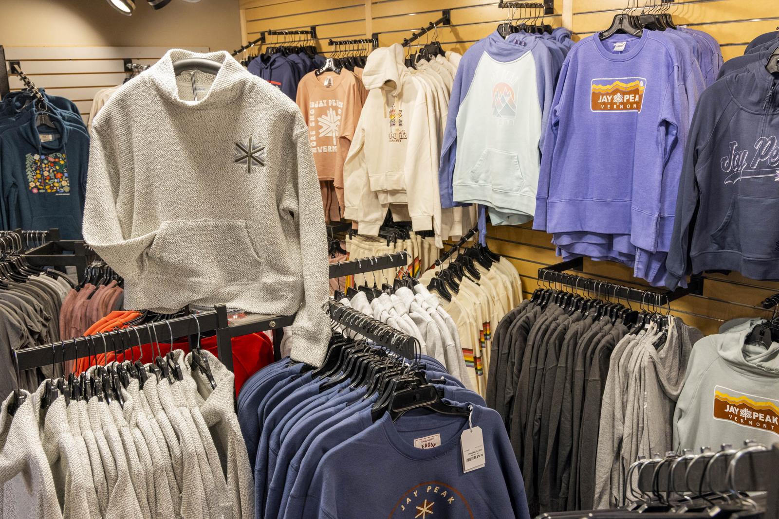 Clothing store display with various sweatshirts on hangers and shelves.