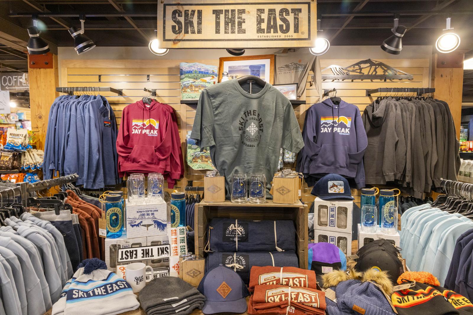Clothing display in a store with hoodies, shirts, and hats under a "Ski the East" sign.