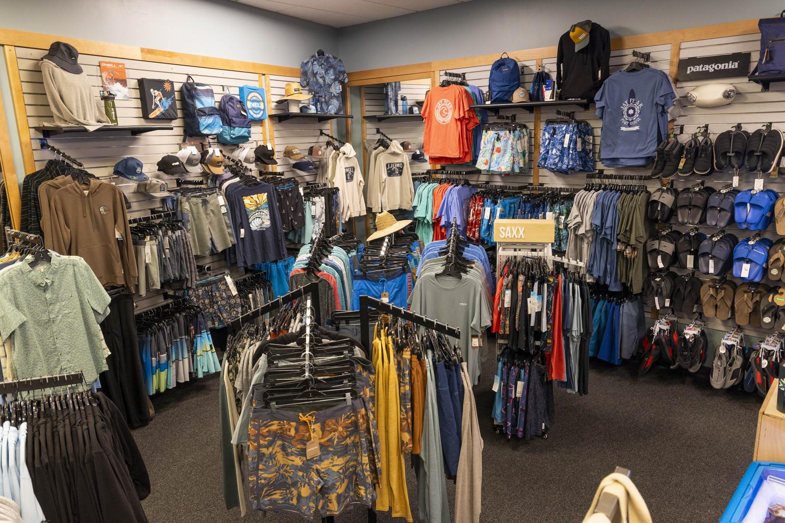 Clothing store interior with racks of shirts, pants, and backpacks.