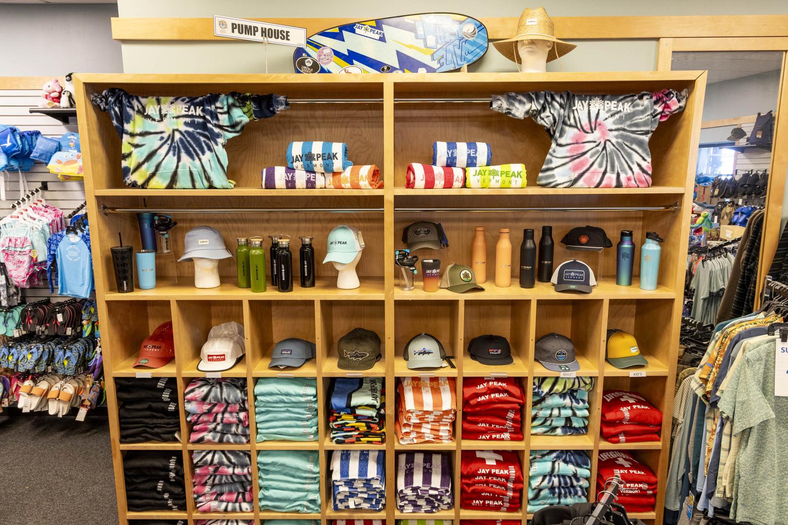 Store display with tie-dye shirts, hats, towels, and drink bottles on shelves.