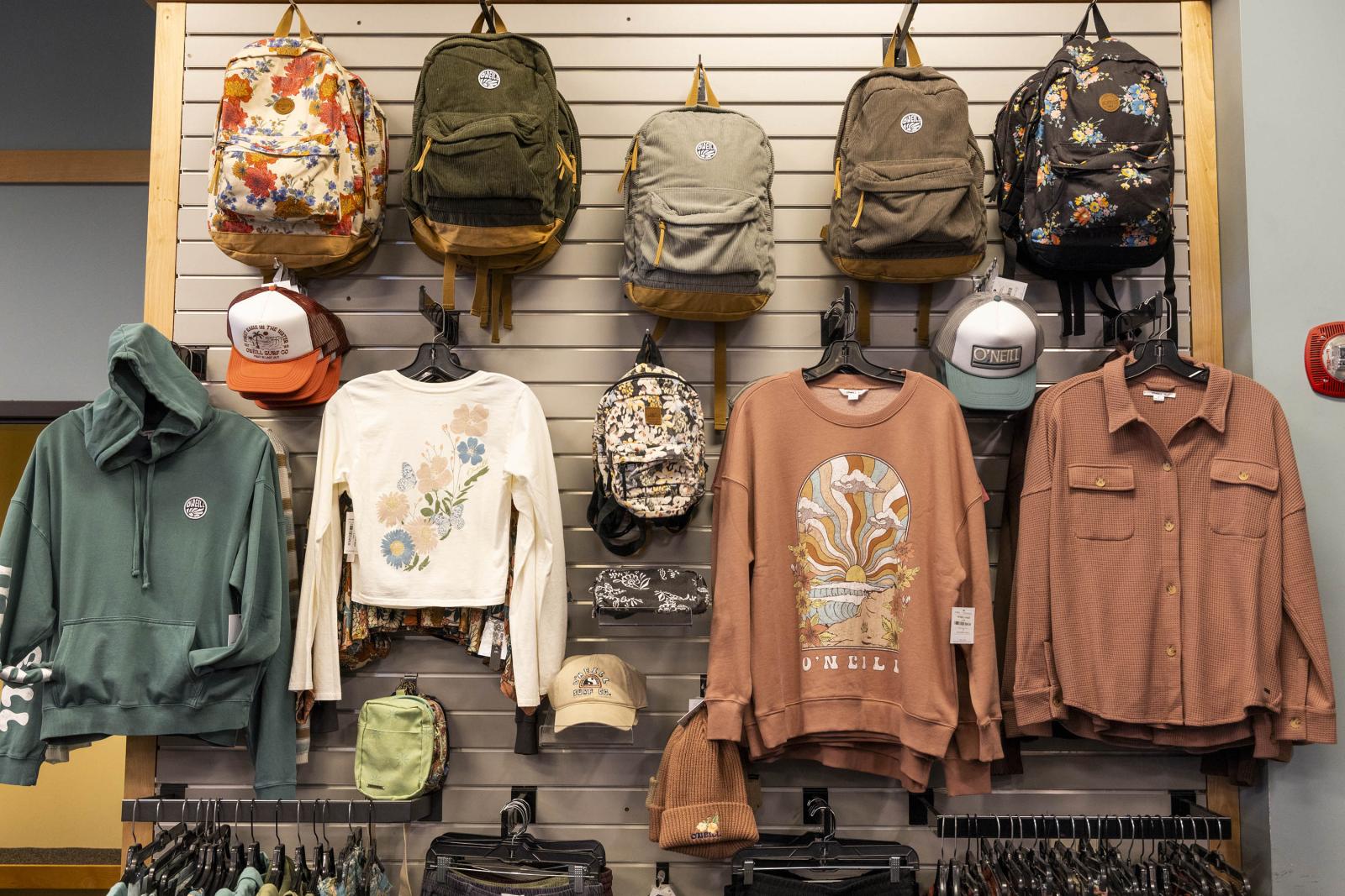 Backpacks, sweatshirts, and caps displayed on a store wall.