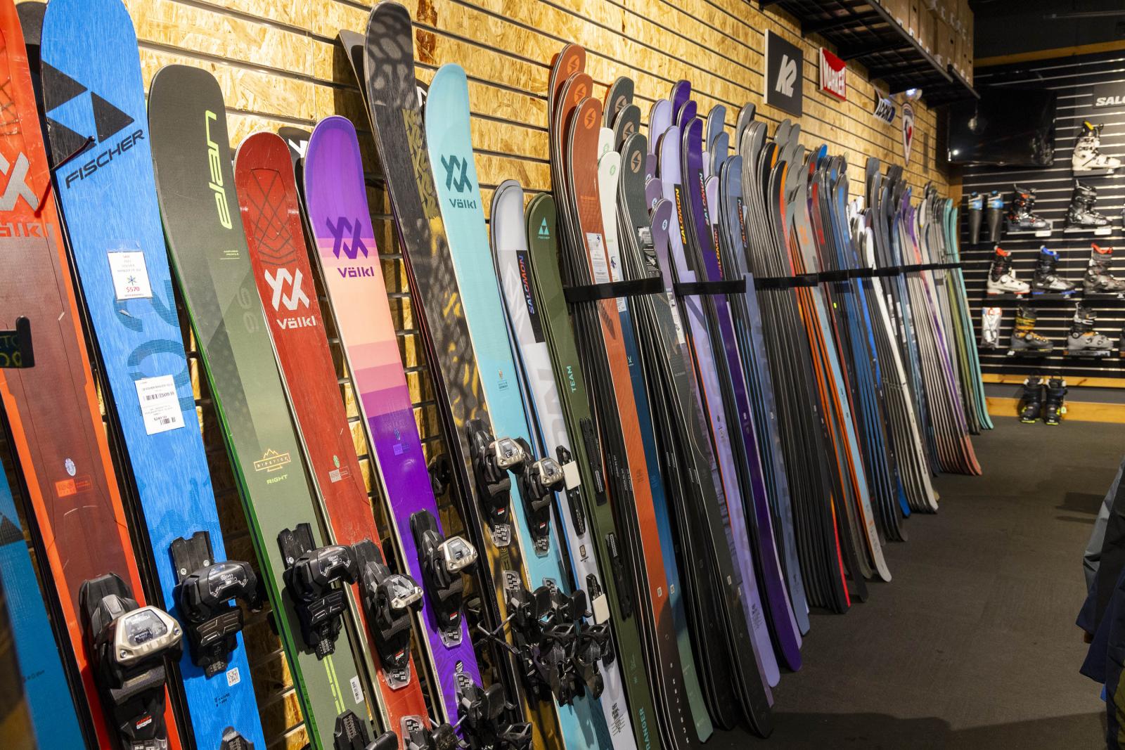 Skis of various colors and brands displayed on a store wall.