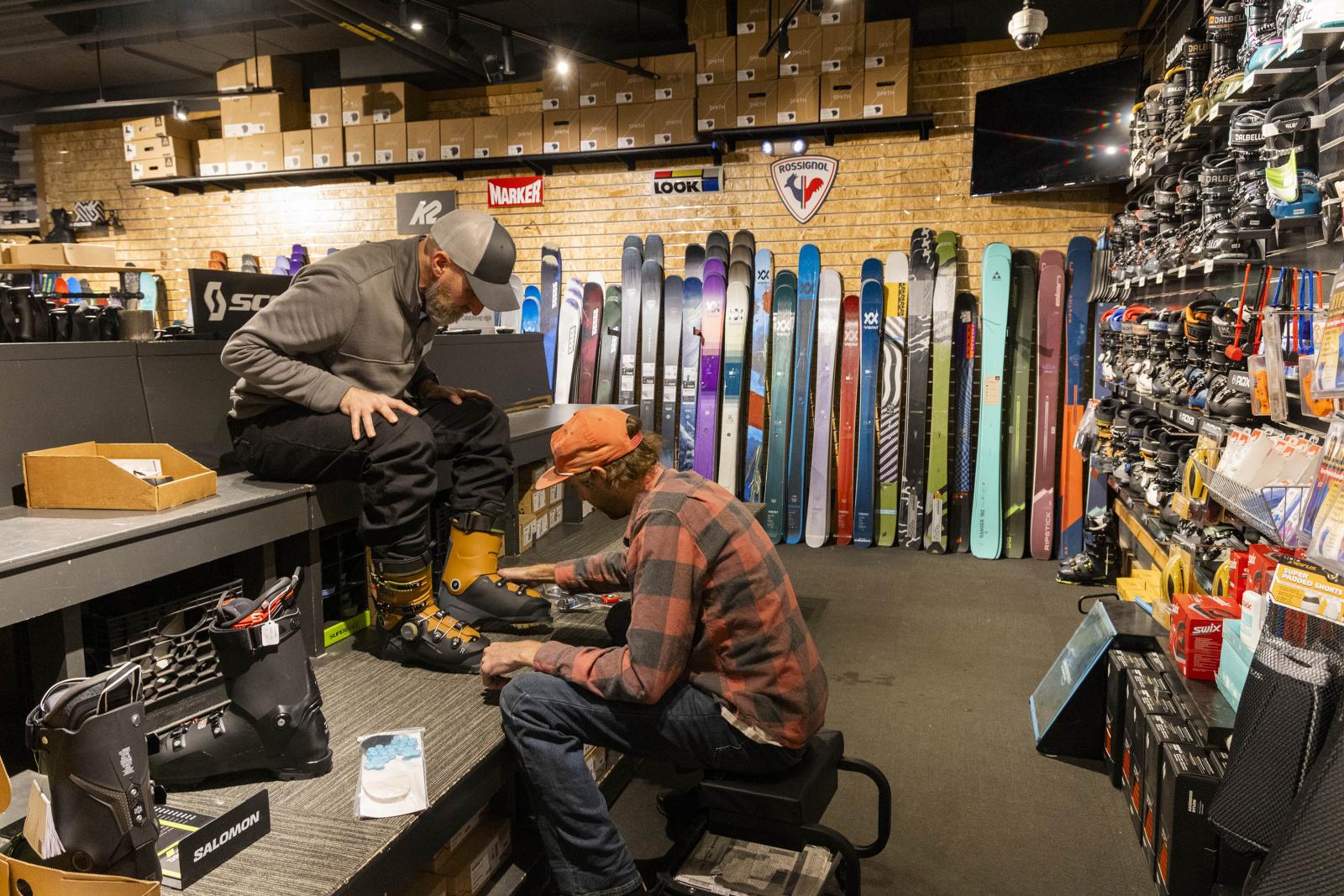 Ski shop; person fitting ski boots, surrounded by colorful skis.