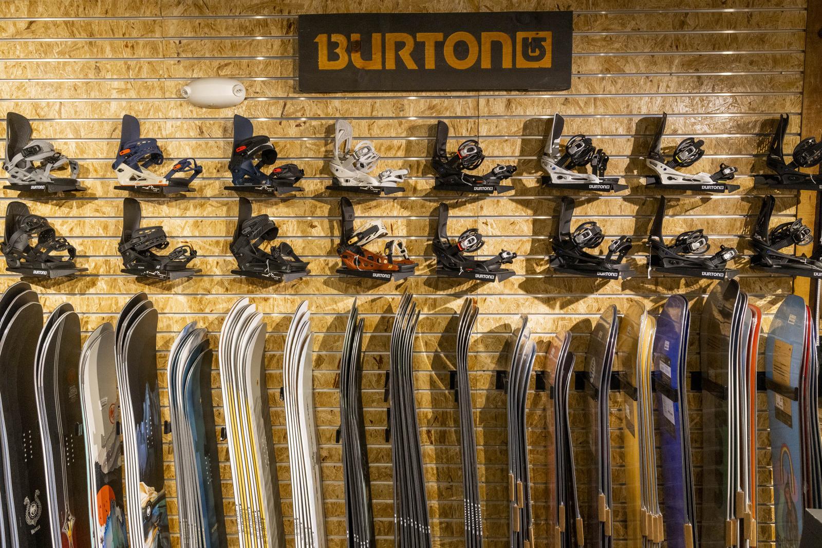 Snowboards and bindings displayed on a brick wall with a Burton logo above.