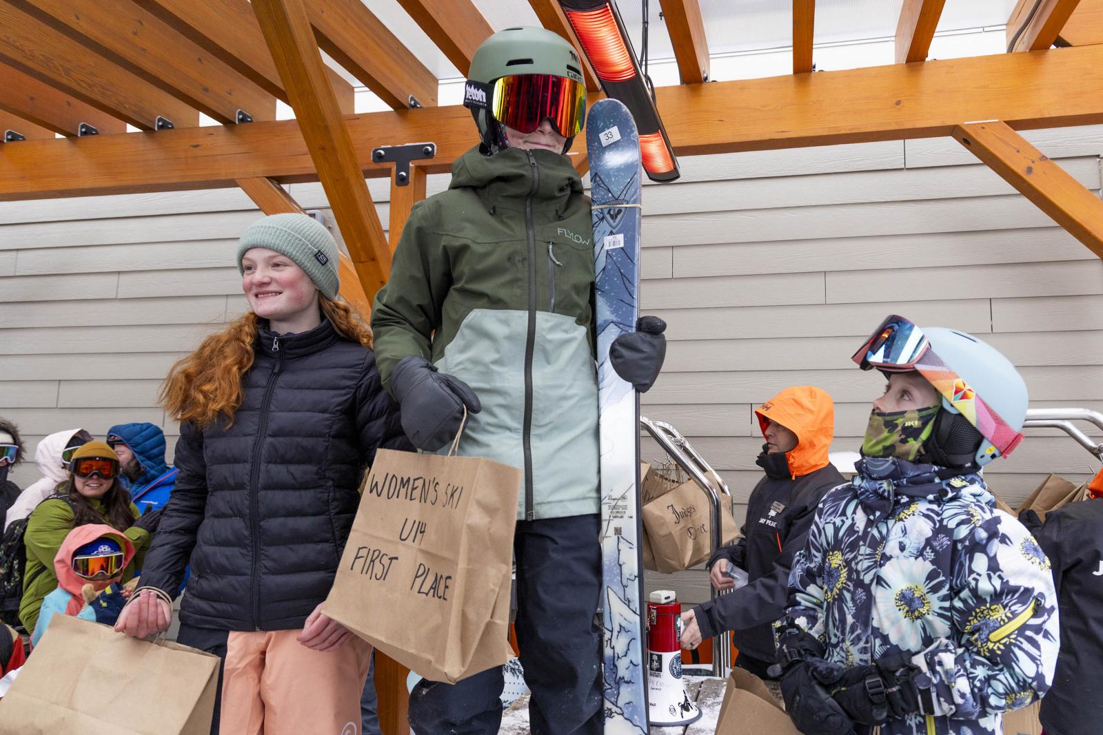 Snowboarders on a podium celebrating under a wooden roof.
