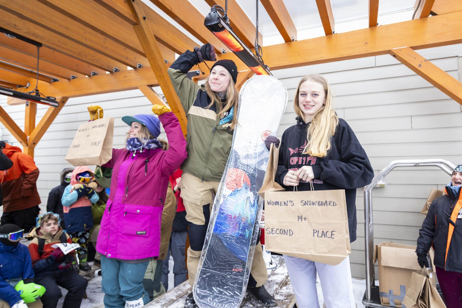 Snowboarders celebrating on a podium in a snowy outdoor setting.