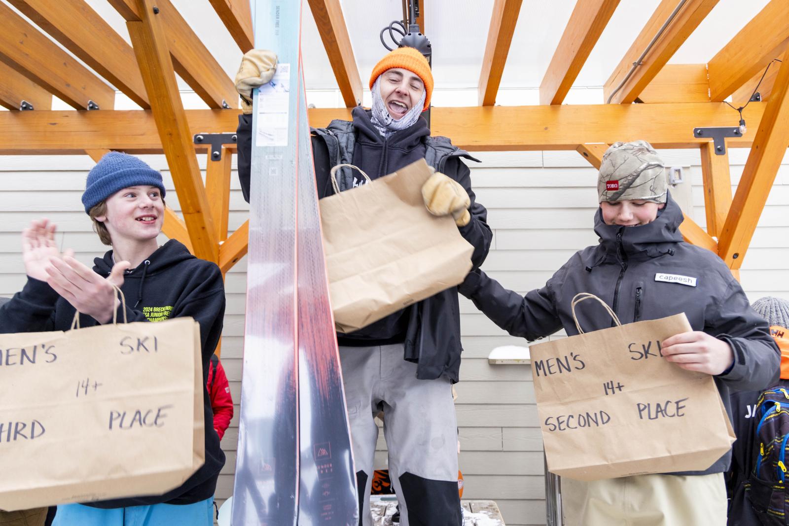 Three people celebrating, holding paper bags, under a wooden roof.