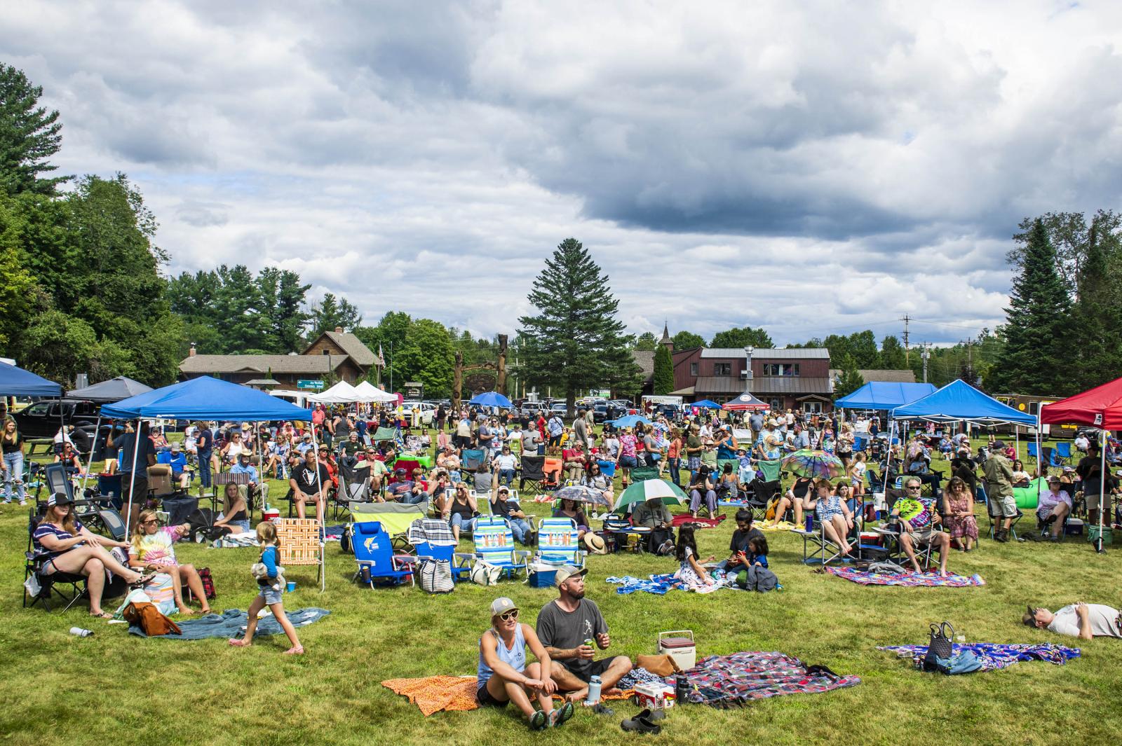 Outdoor festival with a crowd on a grassy area, cloudy sky above.