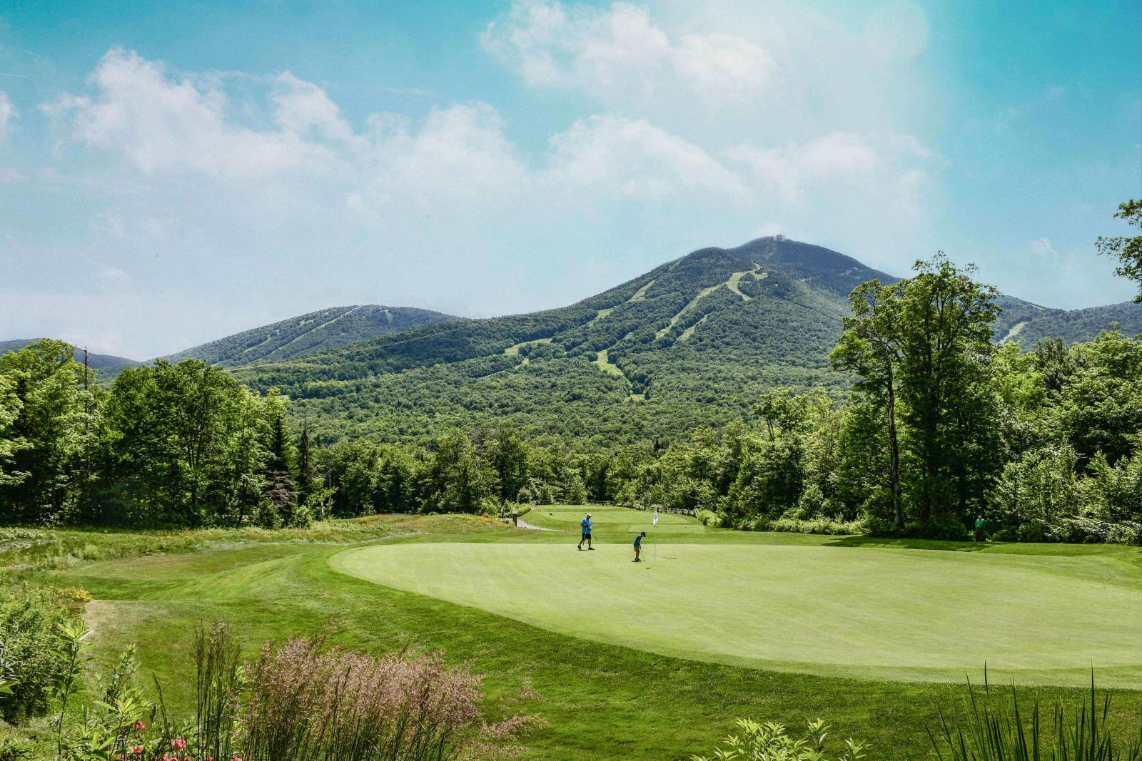 Golf course with mountains in the background under a blue sky.