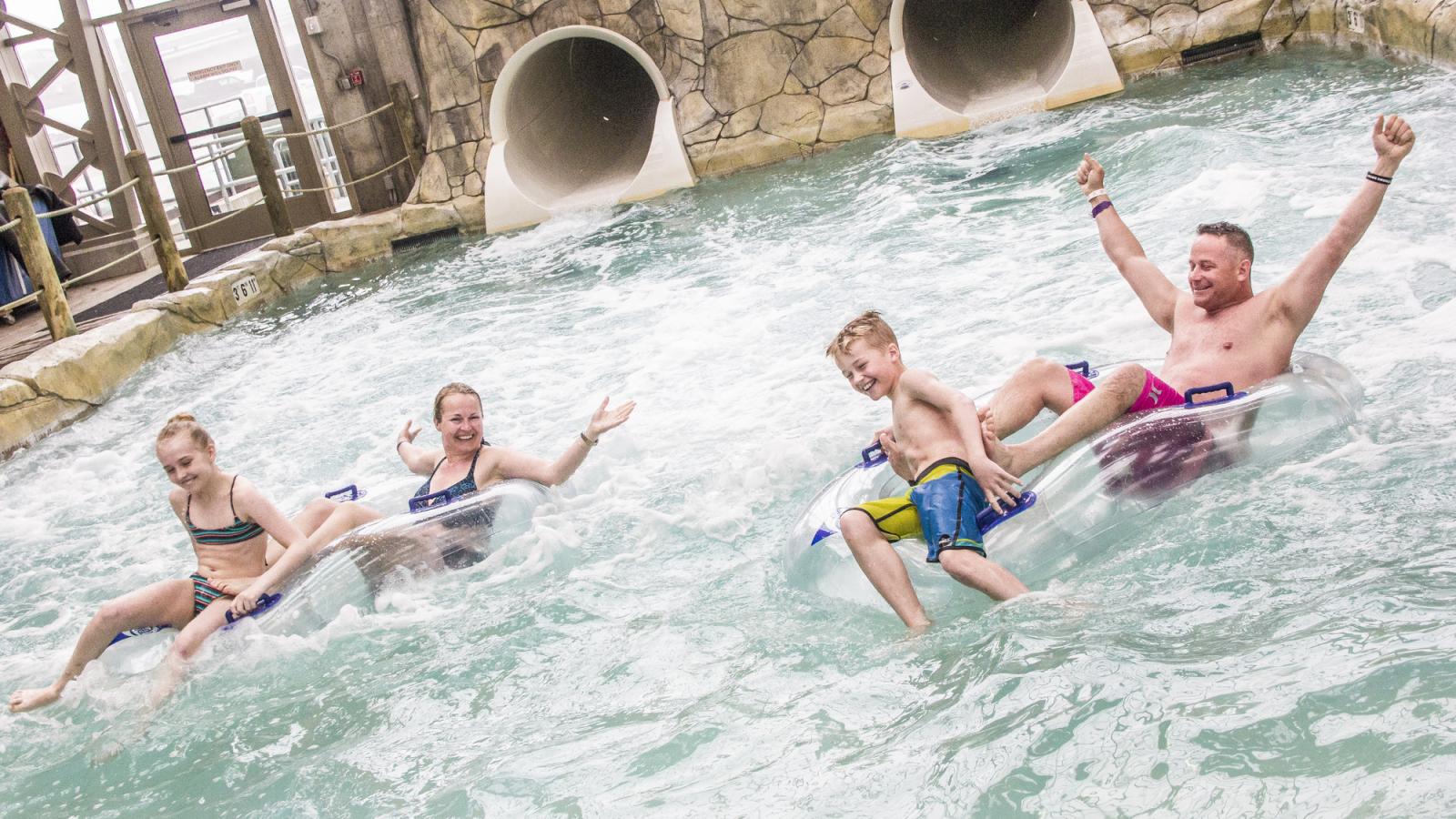 Group enjoying water ride on inflatable tubes, raising arms in excitement.
