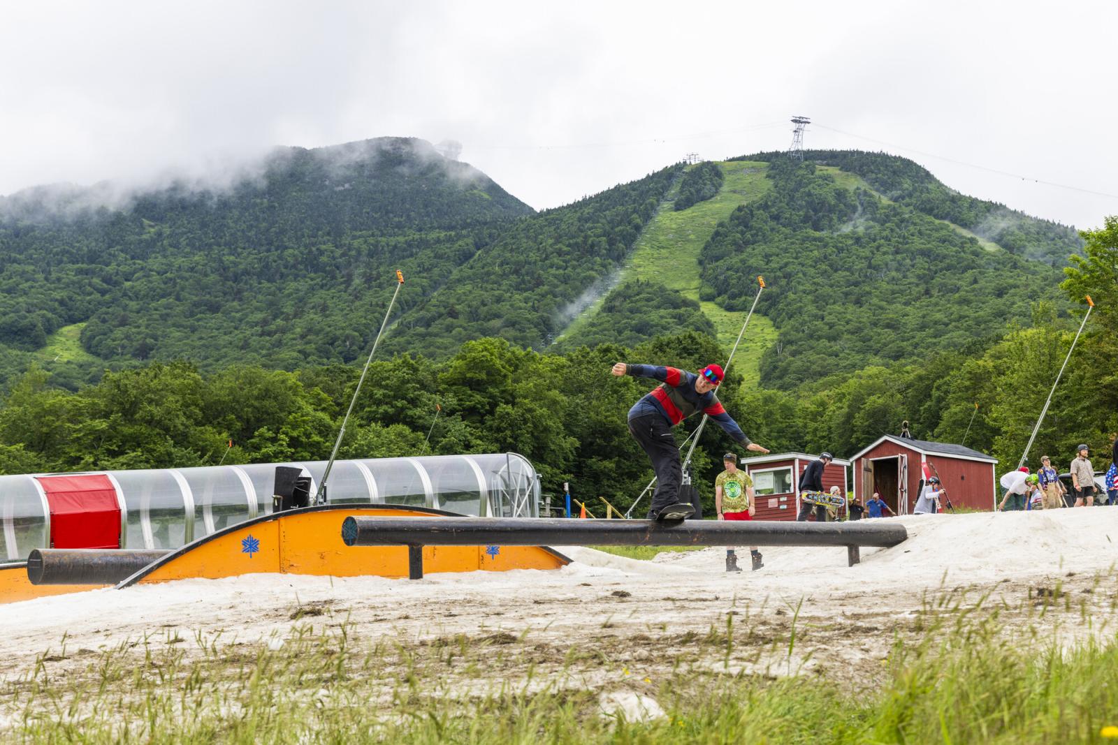 Skateboarder balancing on a rail in a mountainous outdoor park.