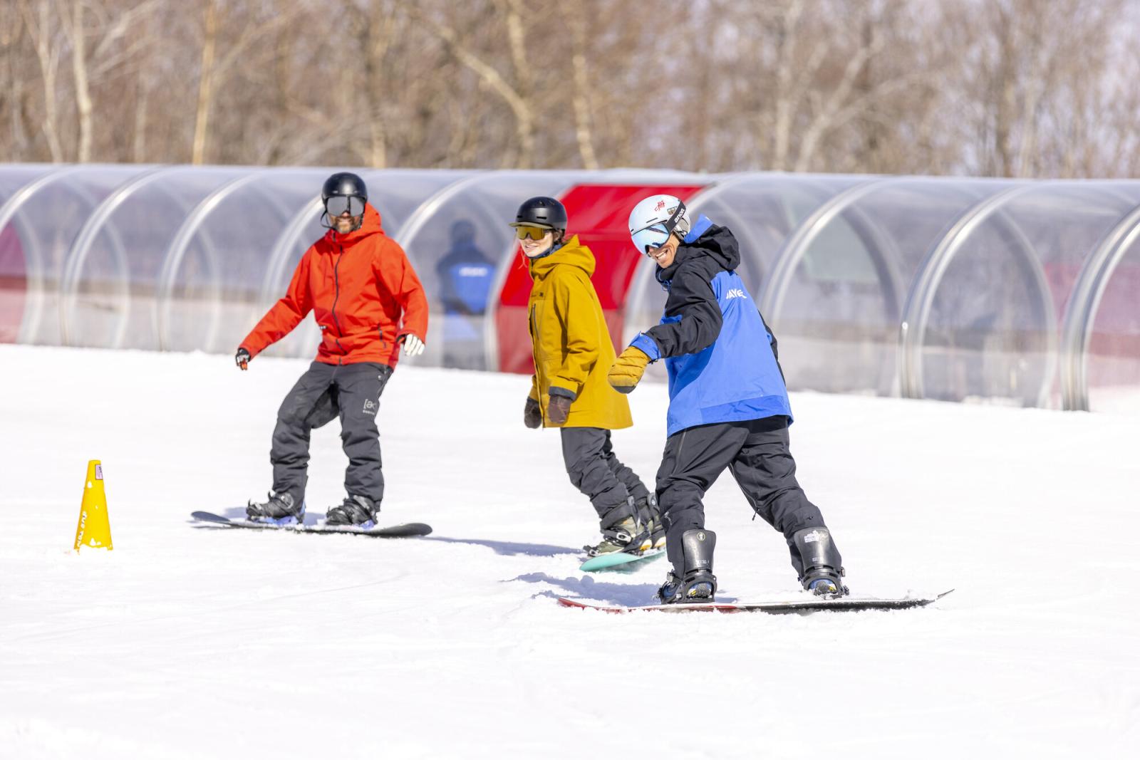 Three snowboarders on a snowy slope, wearing colorful jackets.