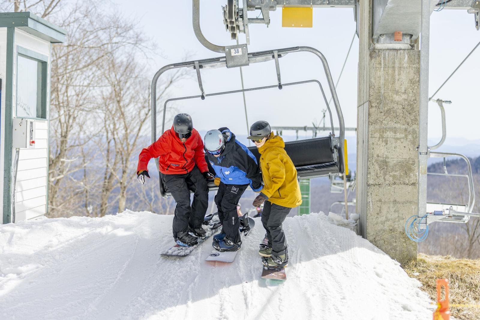 Three snowboarders in colorful jackets near a ski lift on a snowy slope.
