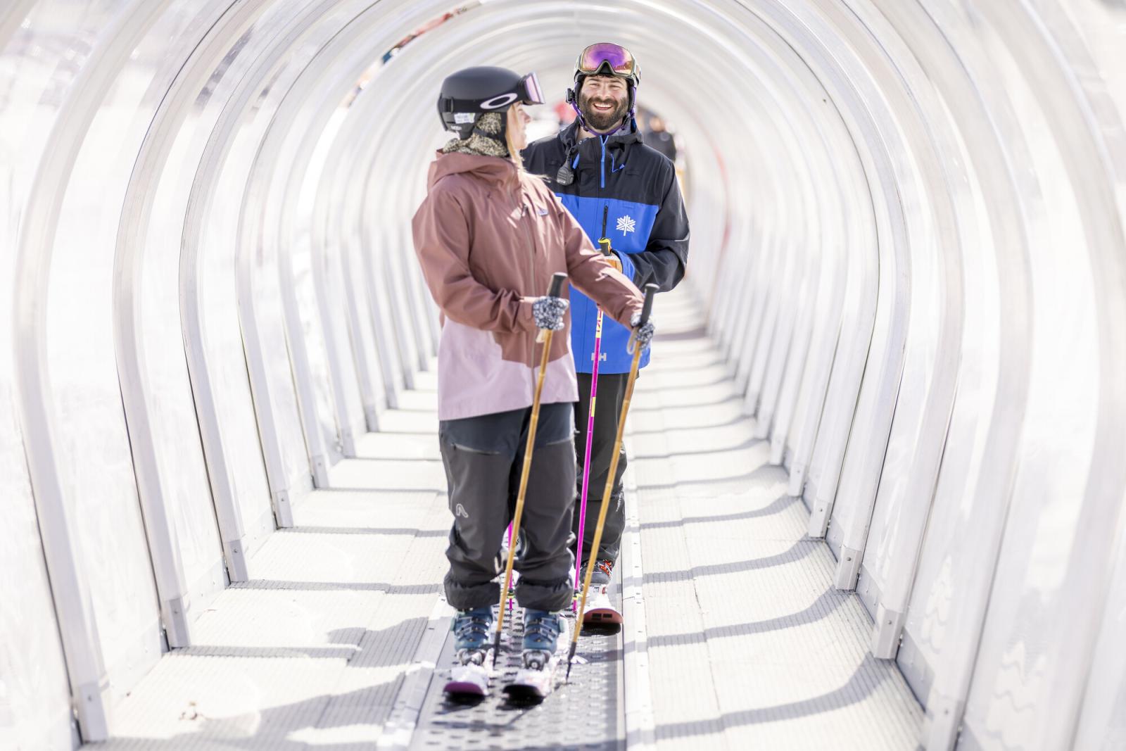 Skiers on a tunnel escalator at a ski resort.