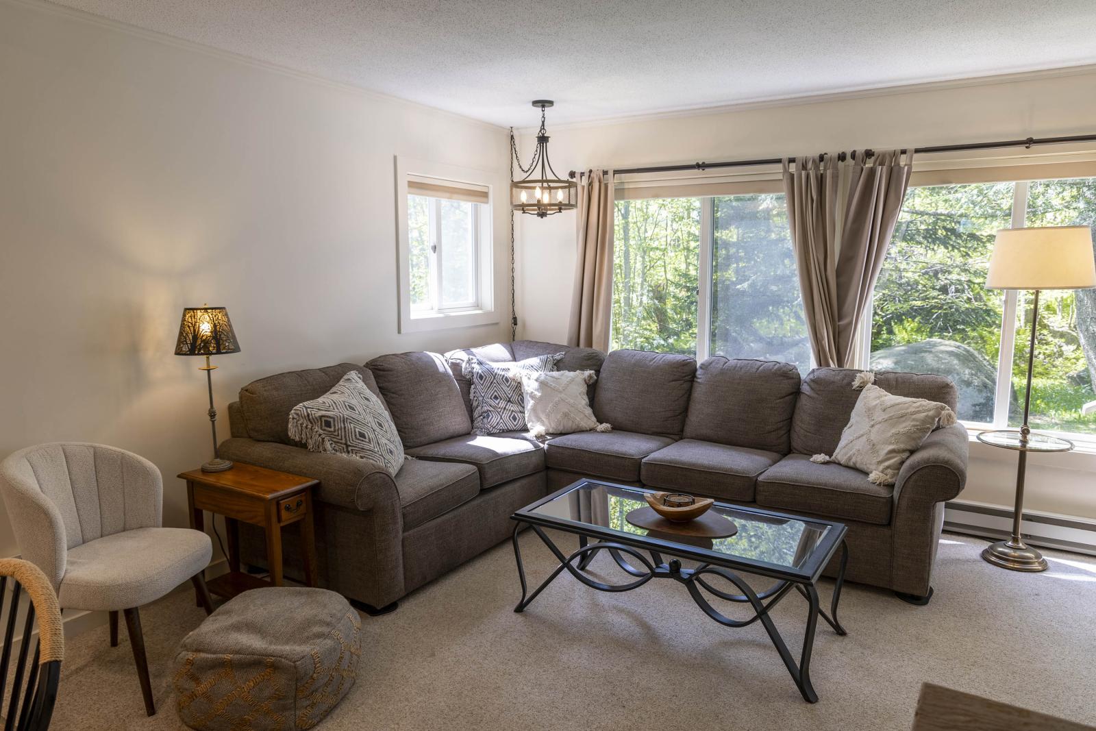 Cozy living room with gray sectional sofa, glass coffee table, and large windows.