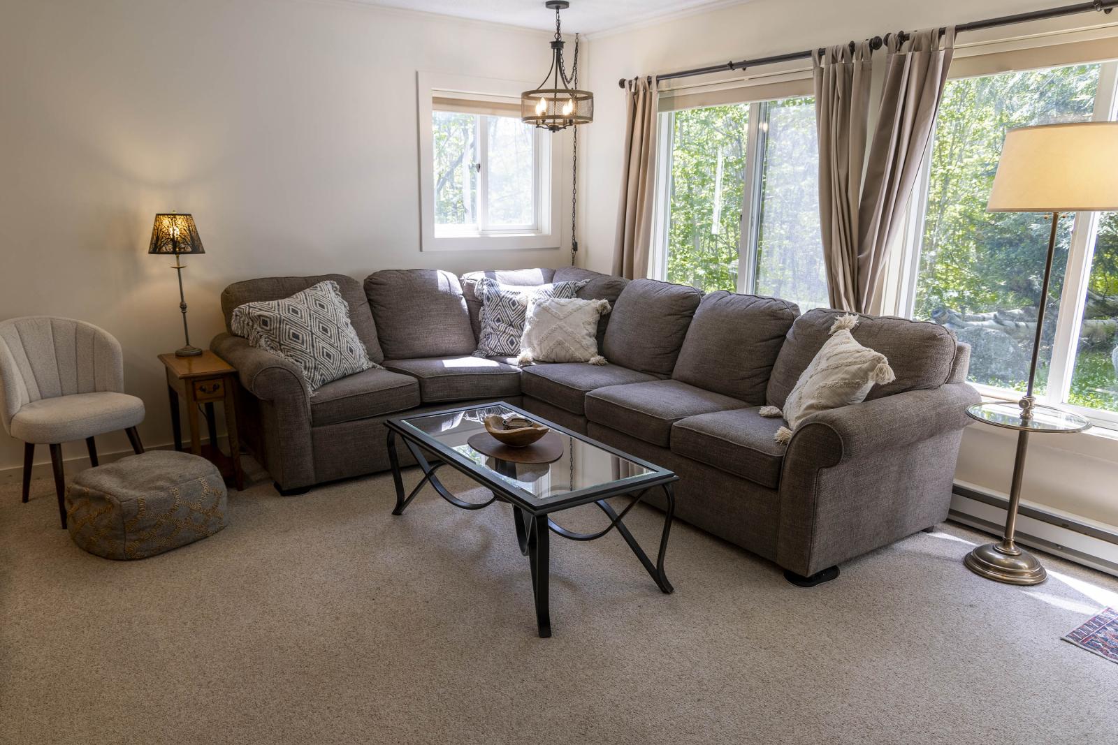 Cozy living room with a gray sectional sofa, glass coffee table, and large windows.