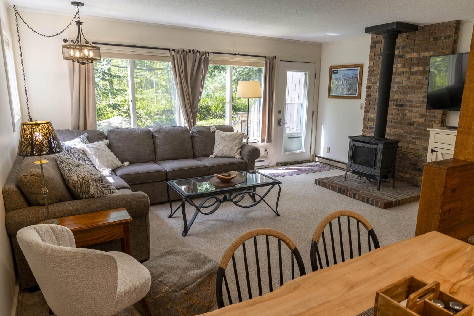 Cozy living room with a grey sofa, wood stove, and large window.
