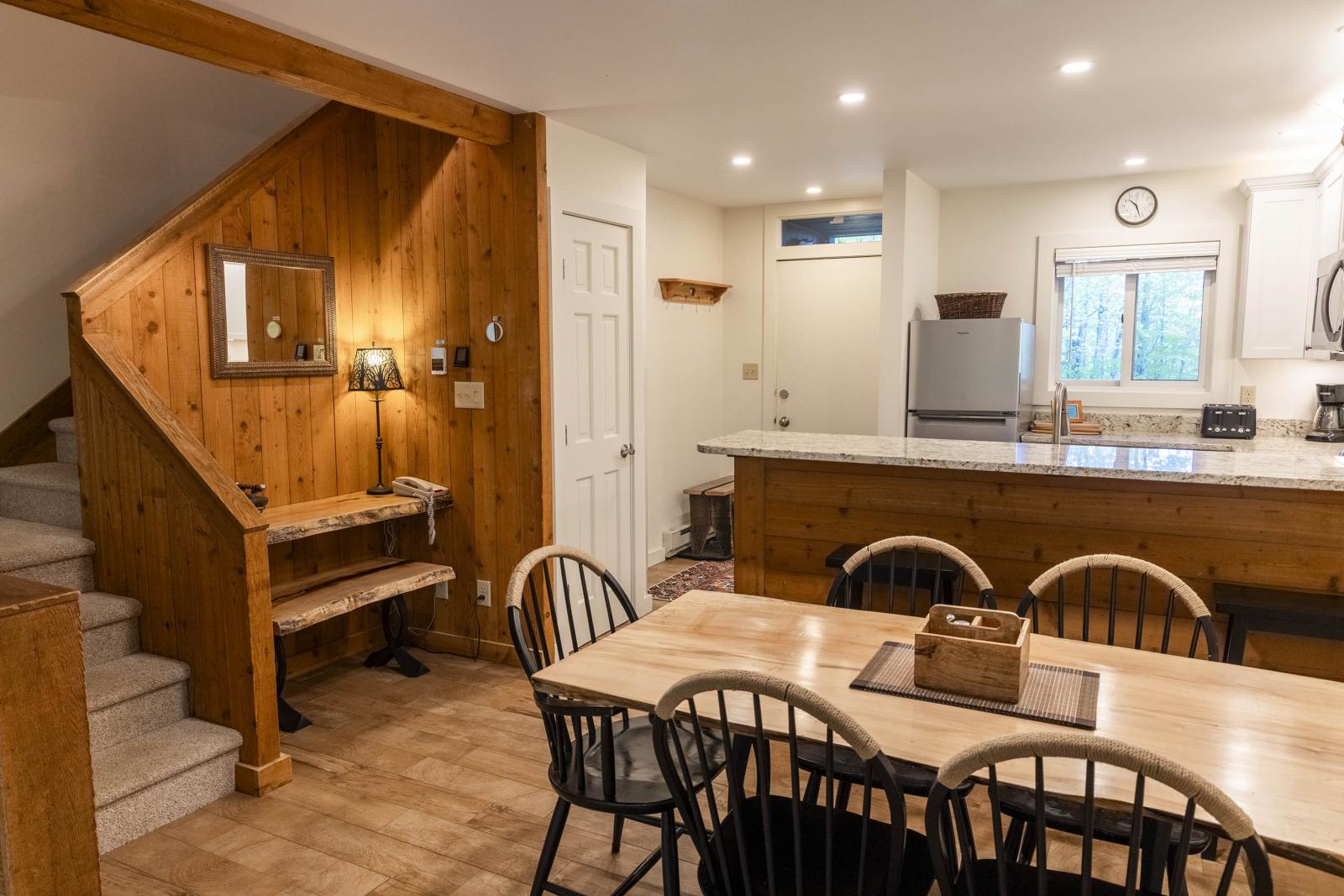 Cozy kitchen with wooden dining table, chairs, and staircase.