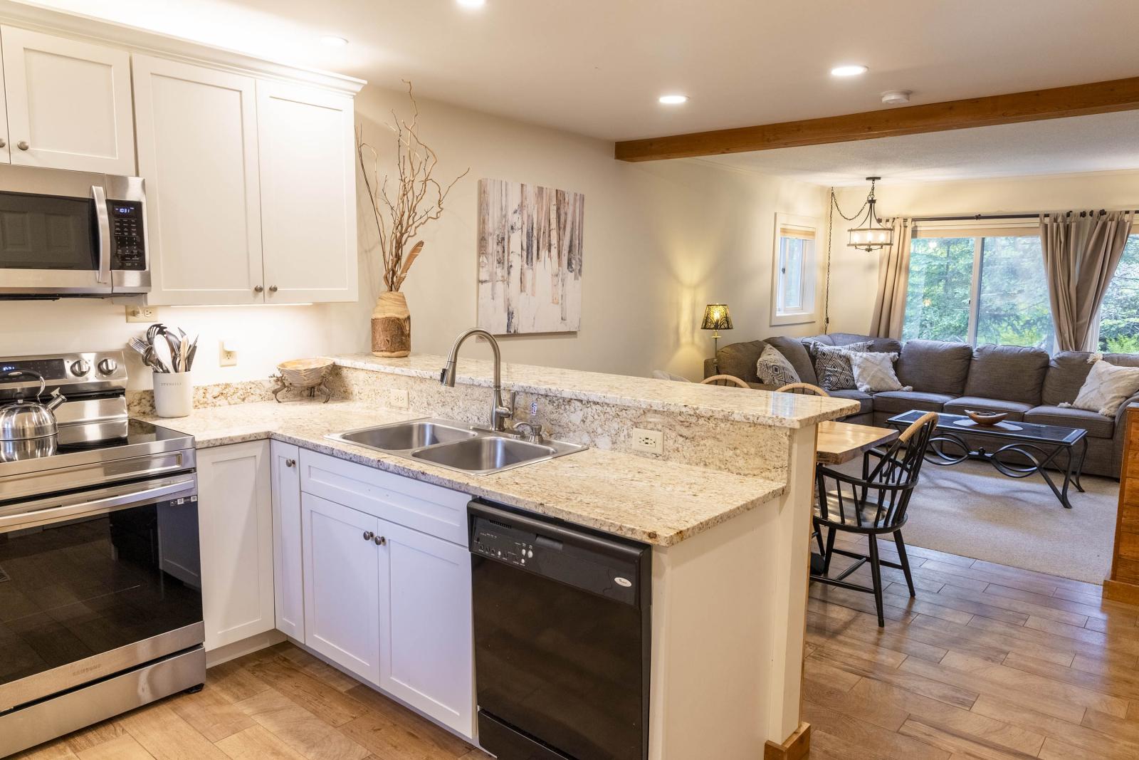 Bright kitchen with white cabinets, granite counters, and open view to a cozy living room.