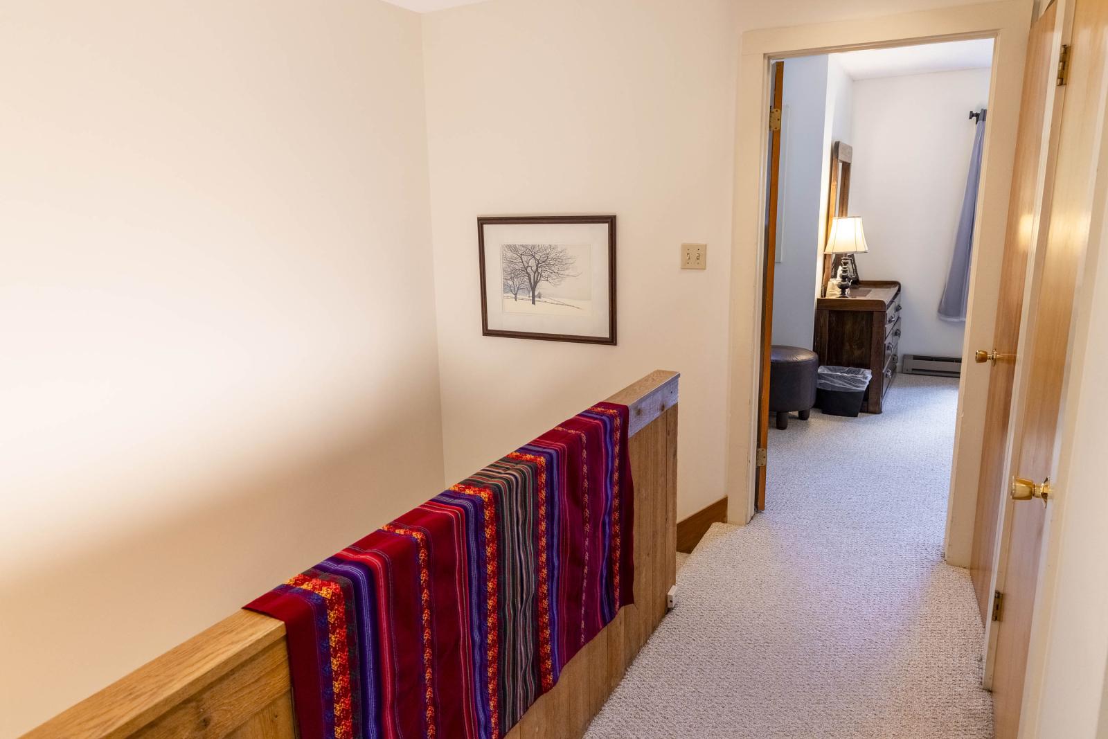 Hallway with colorful scarves on railing, leading to a room with a lamp and window.