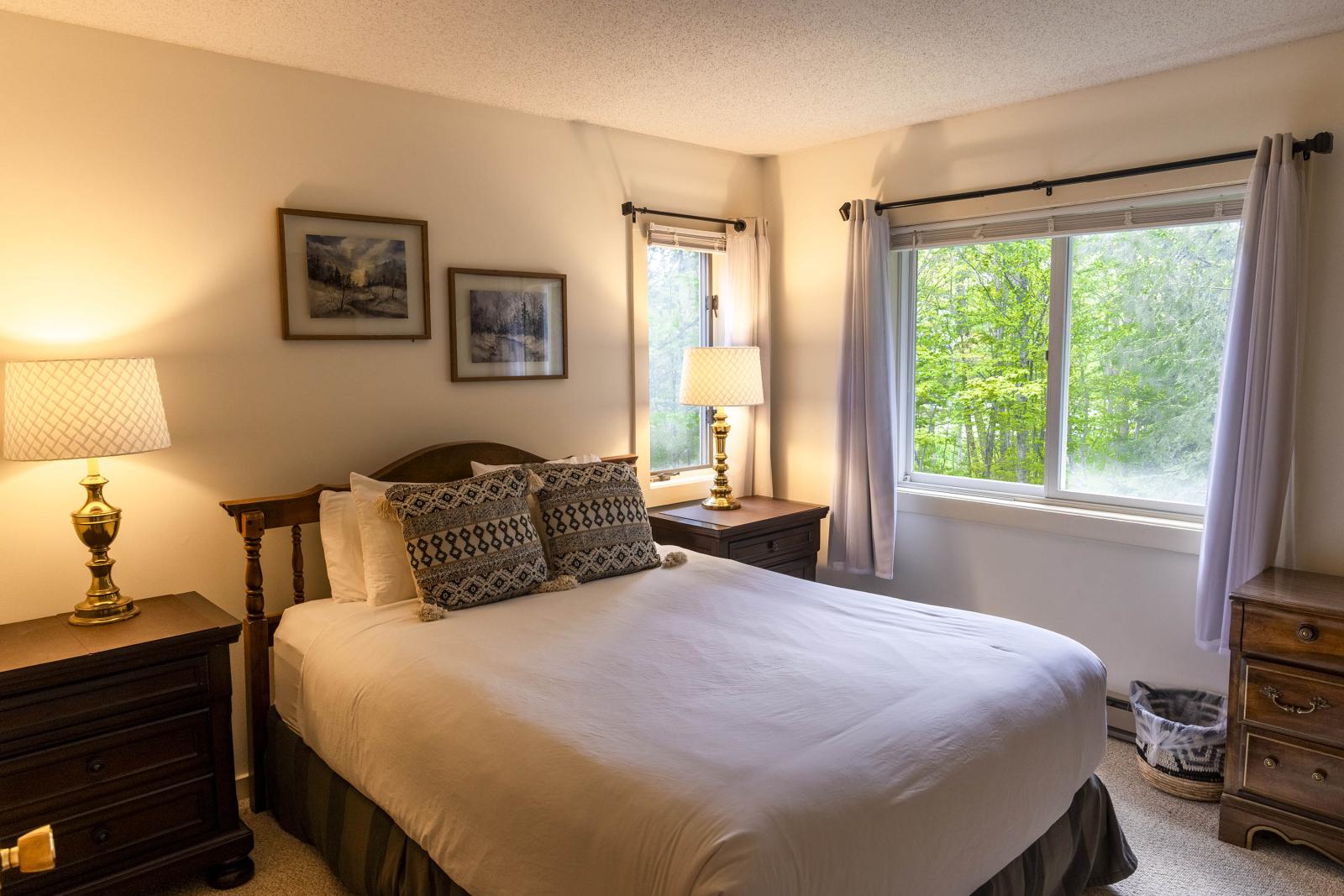 Cozy bedroom with double bed, two lamps, and a window overlooking greenery.