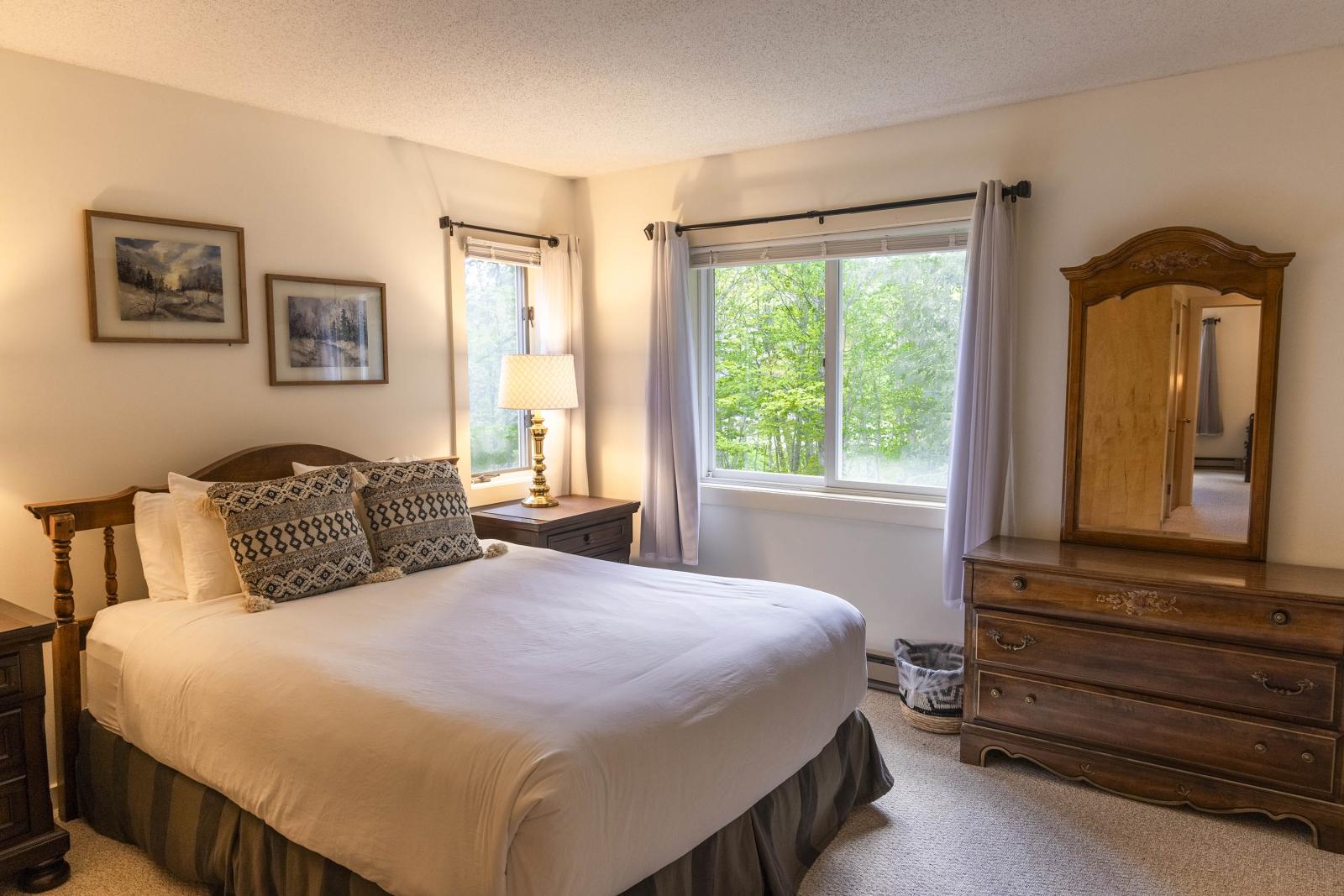 Cozy bedroom with a bed, wooden dresser, and a window with light curtains.