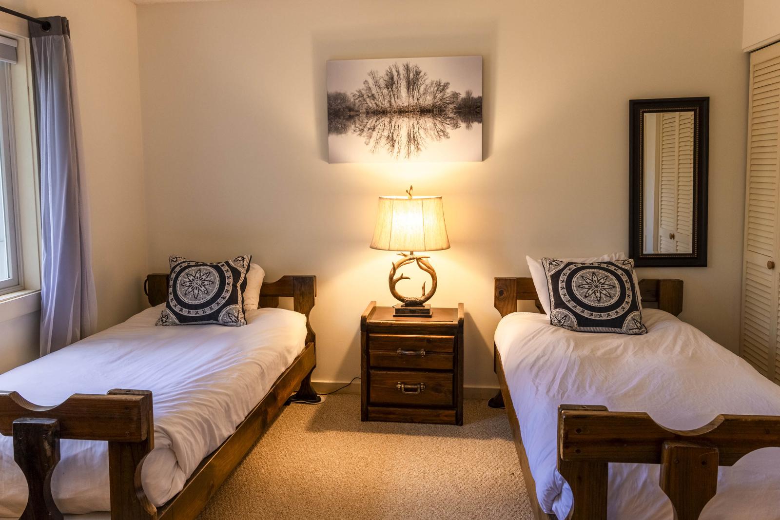 Two beds in a cozy room with a lamp and framed artwork above.