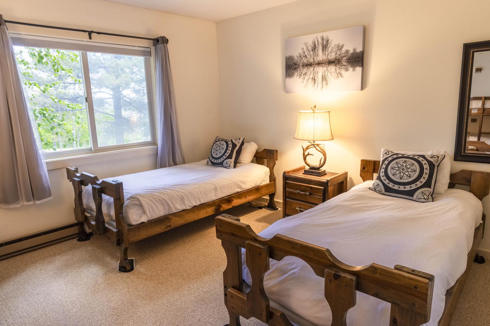Cozy bedroom with two wooden twin beds, a lamp, and a window with curtains.