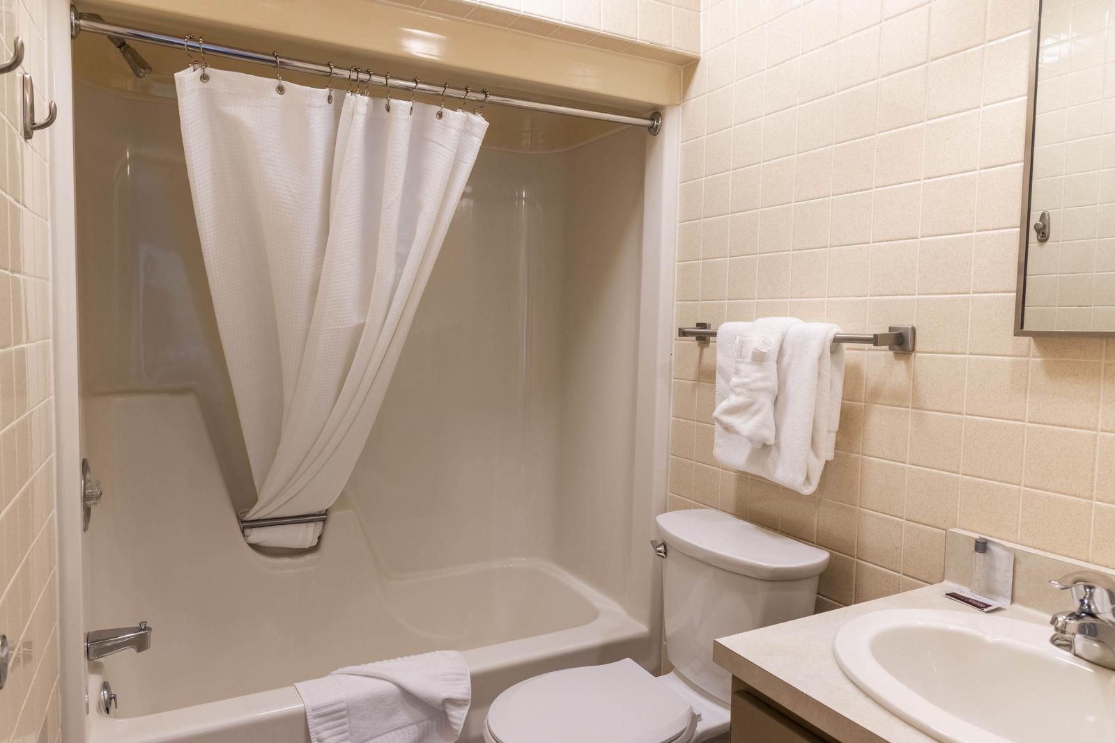 Small beige bathroom with shower, sink, and towel on rack.