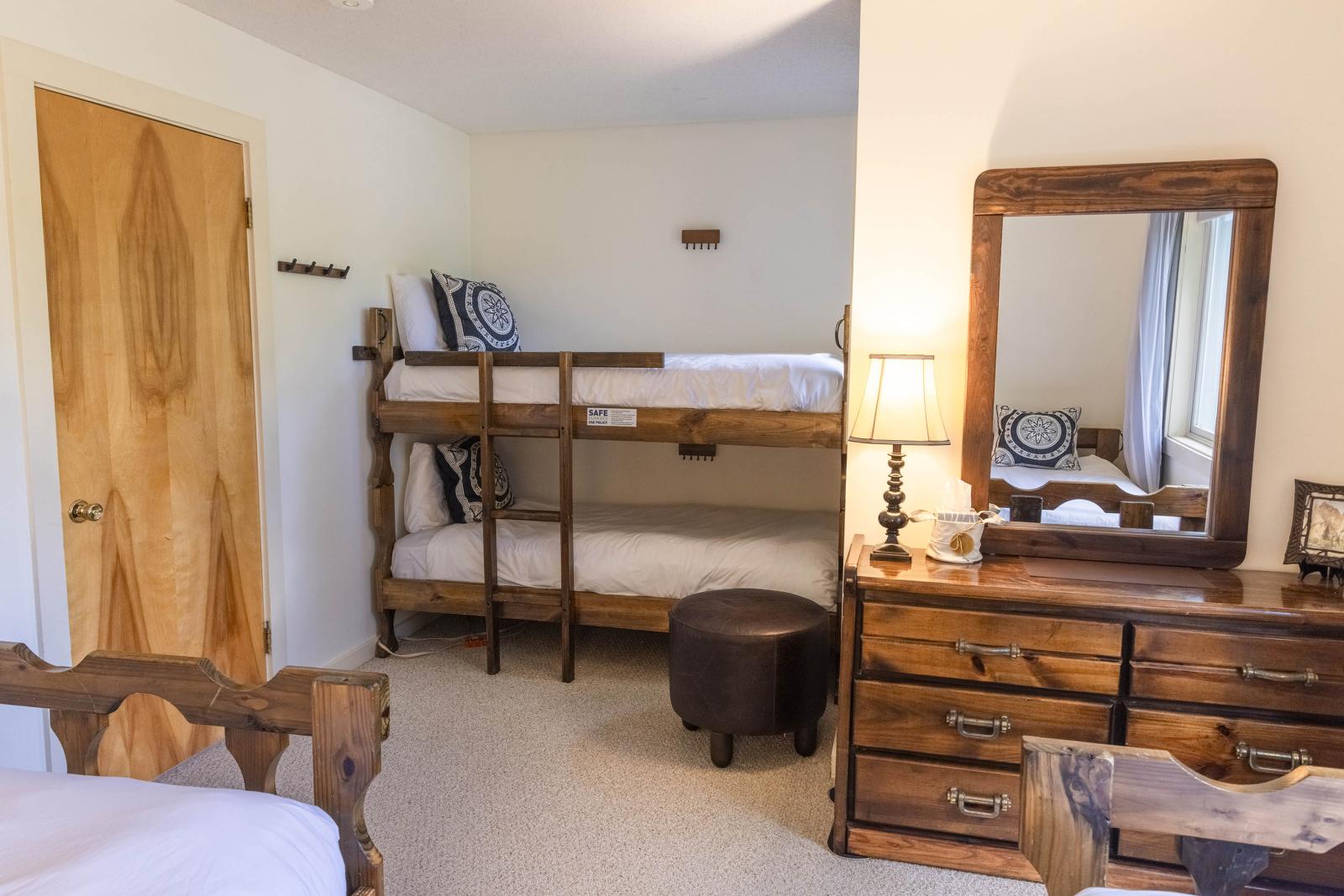 Bedroom with wooden bunk beds, dresser, and a lamp-lit mirror.