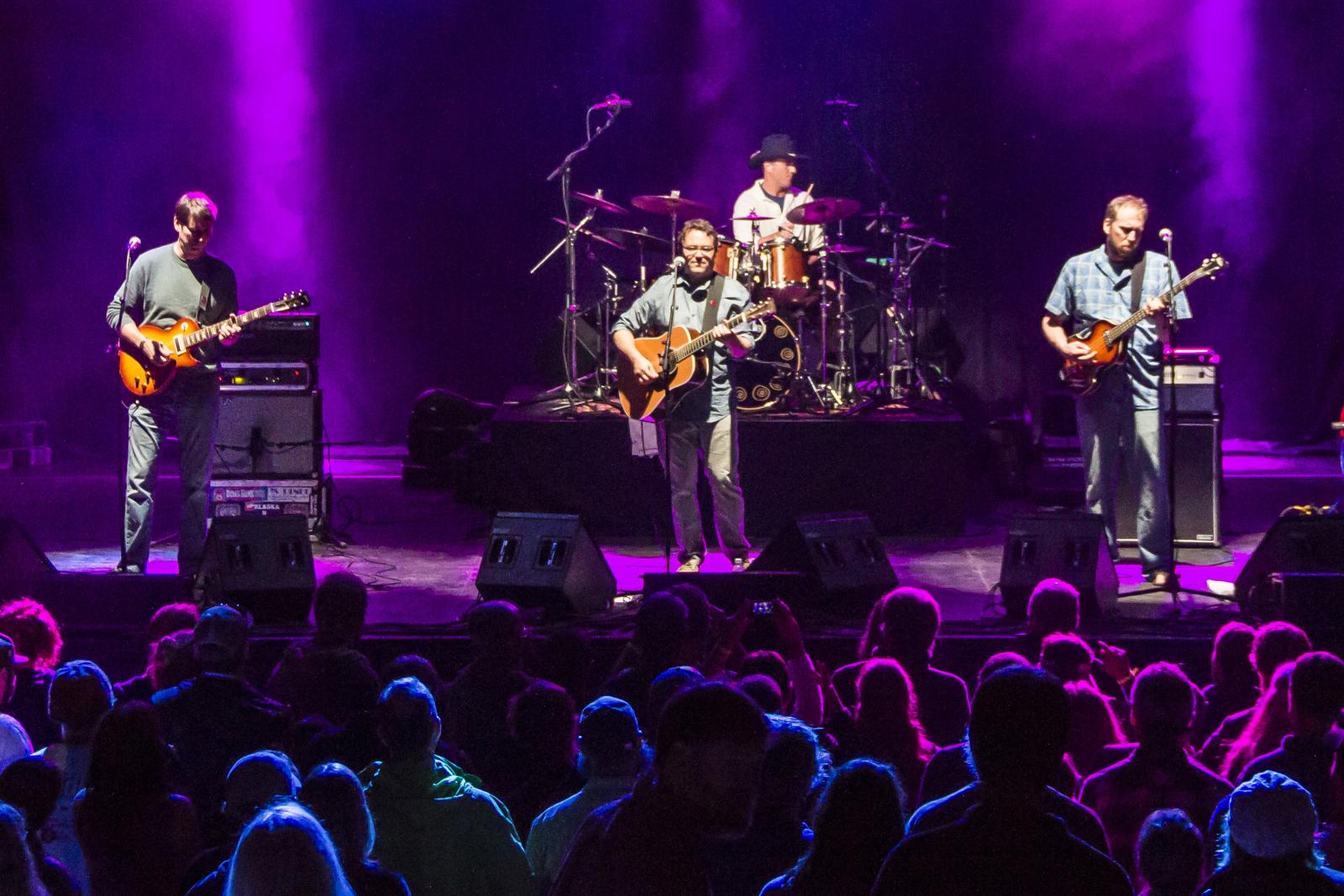 Strangefolk band performing on stage with purple lights and crowd watching.