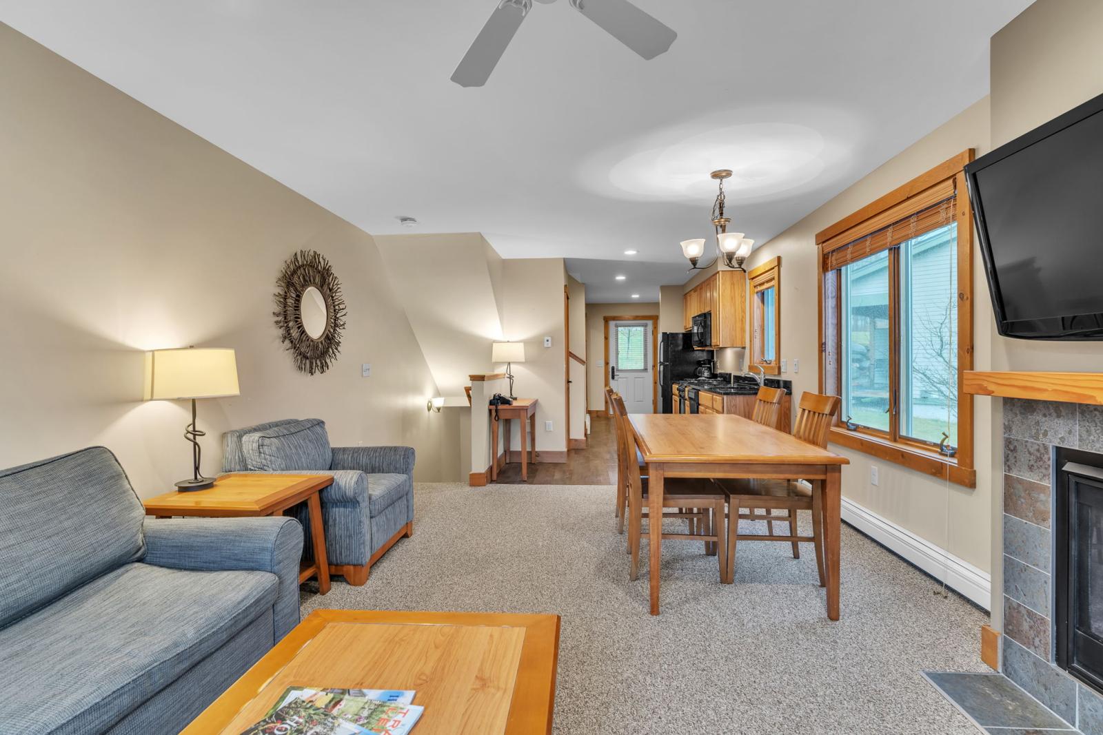 Cozy living room with sofas, wooden table, and TV; kitchen in background.