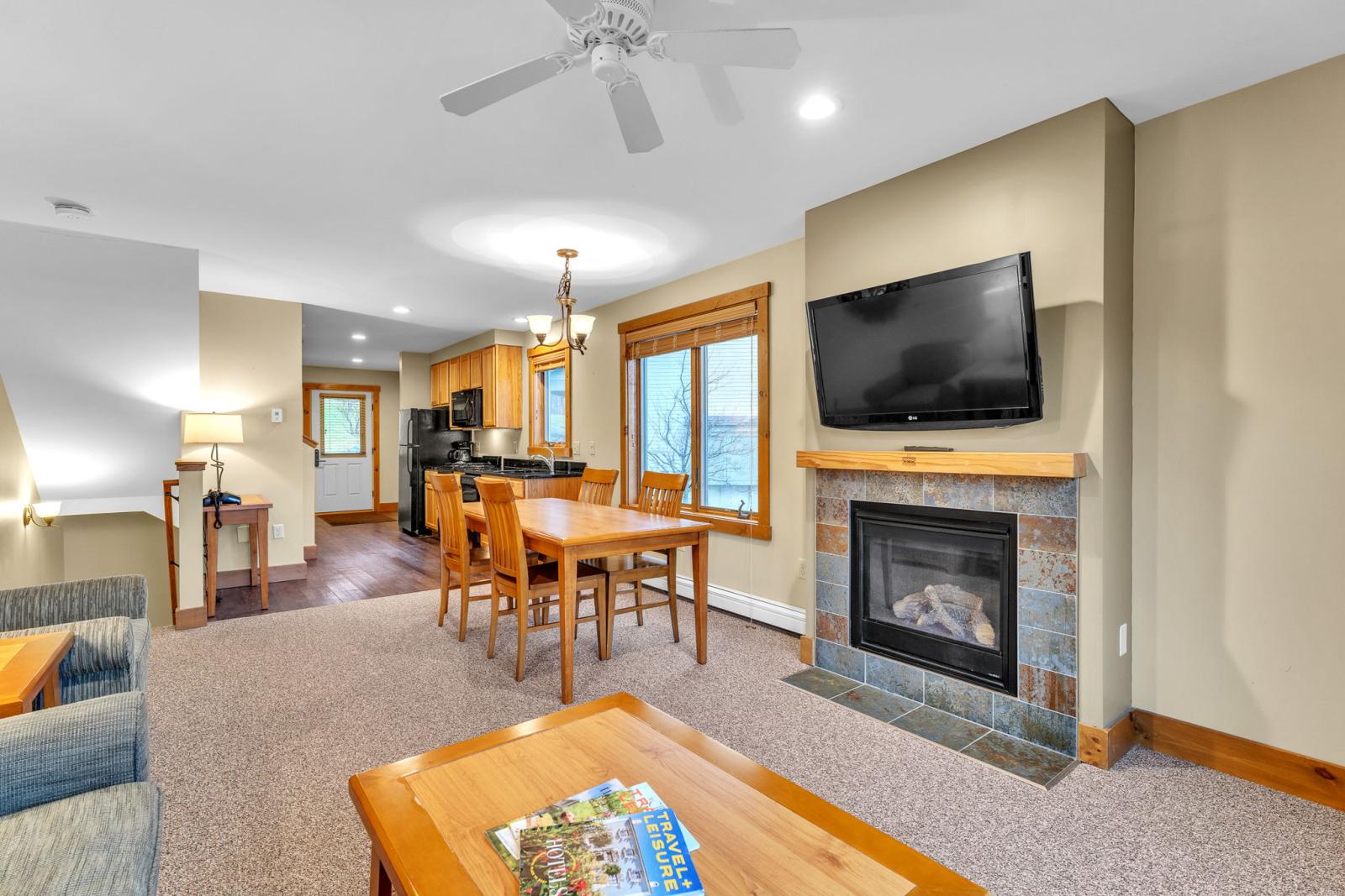 Living room with fireplace, TV, dining table, and kitchen in the background.