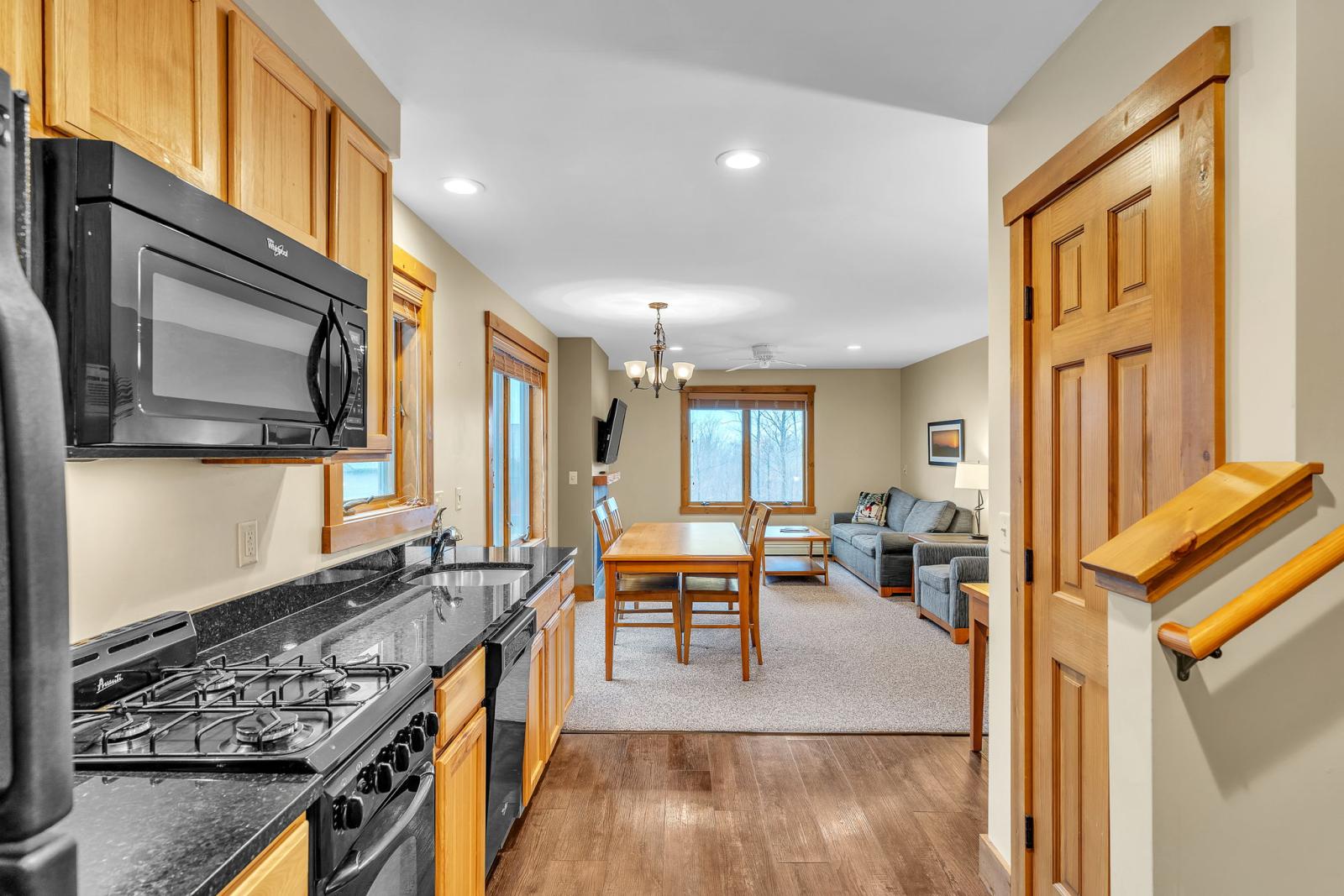 Kitchen and living room, wooden cabinets, black appliances, dining table in center, cozy seating.
