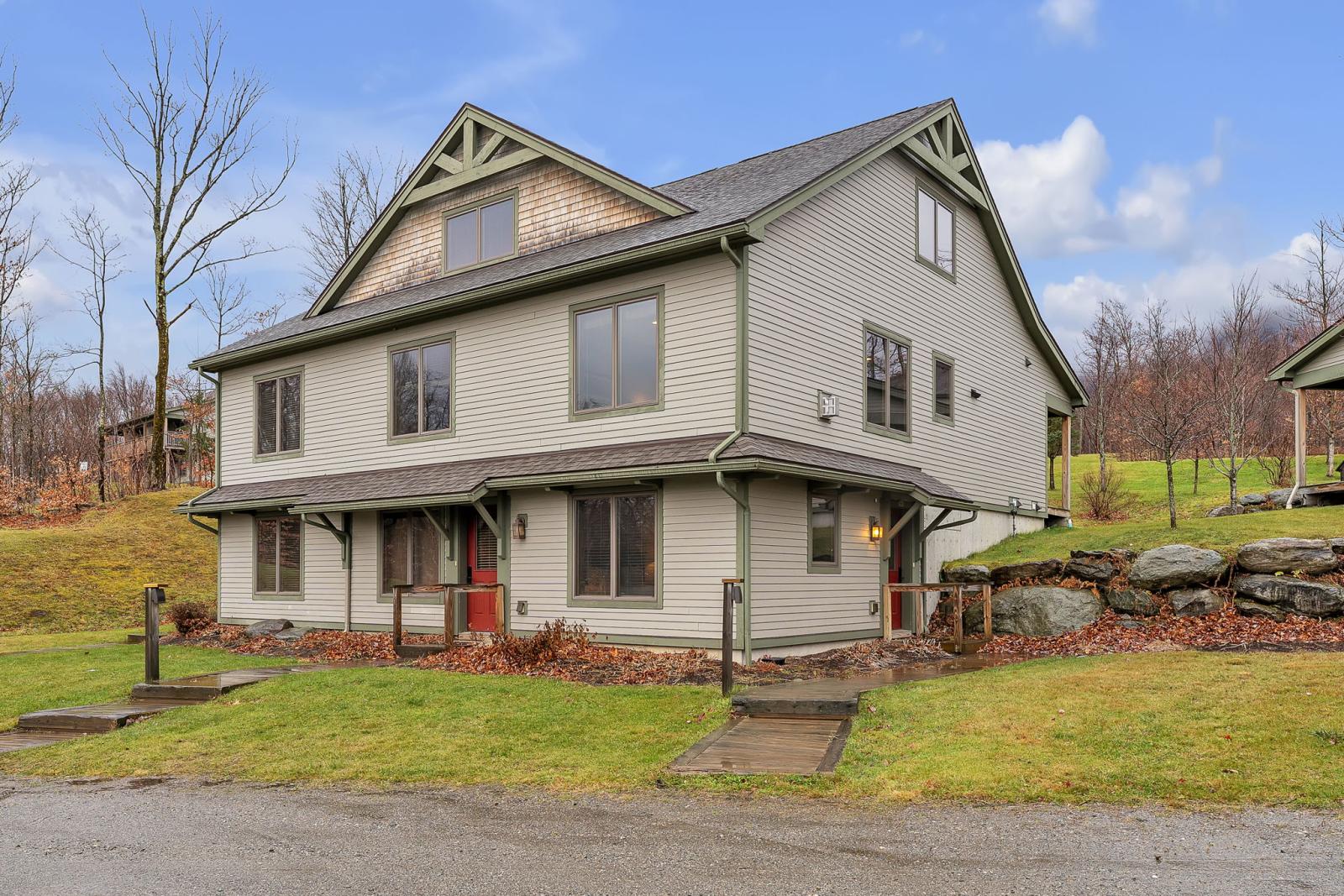 Two-story house with beige siding and green trim in a grassy area.