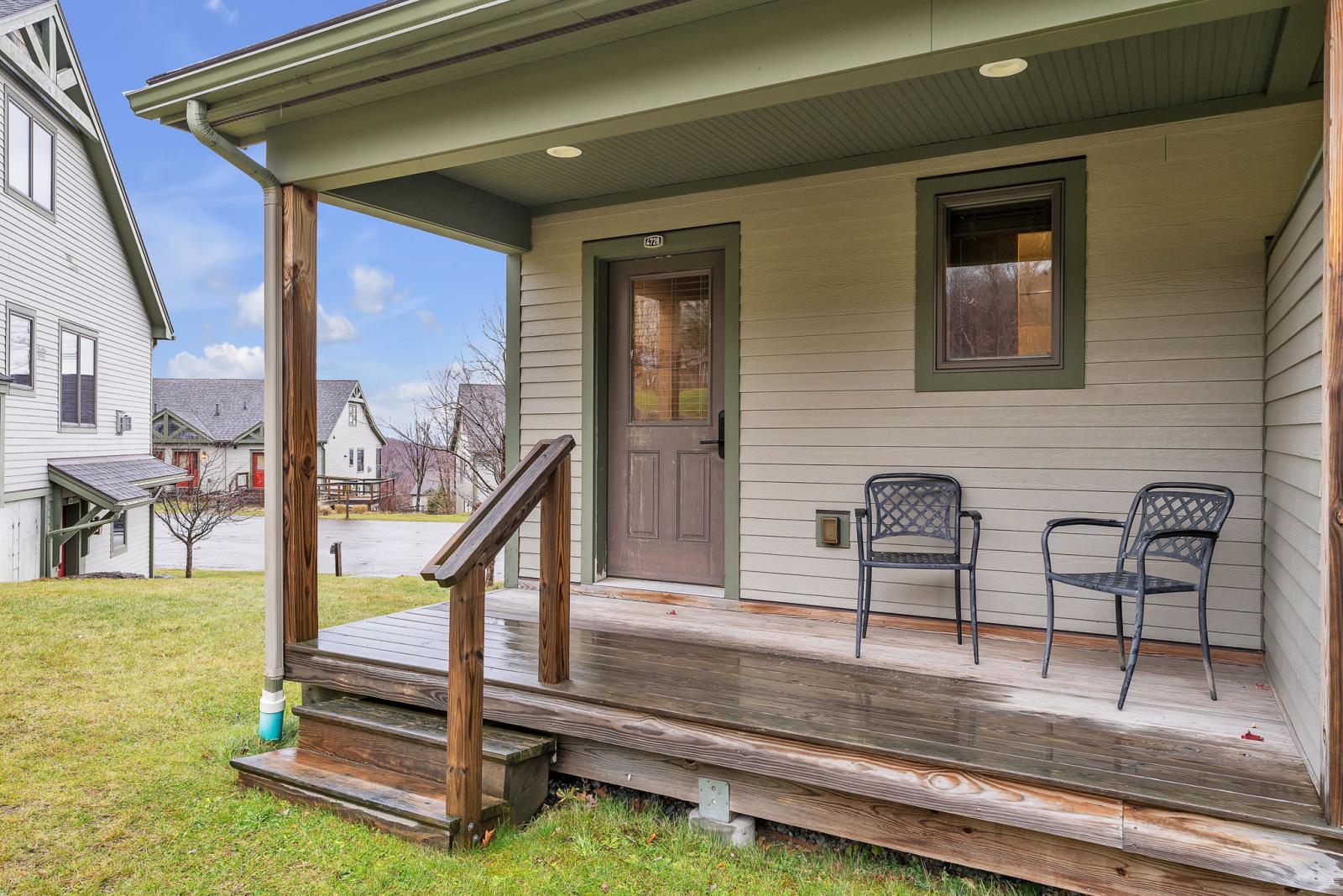 Small porch with two chairs and a wooden railing, overlooking a grassy yard.