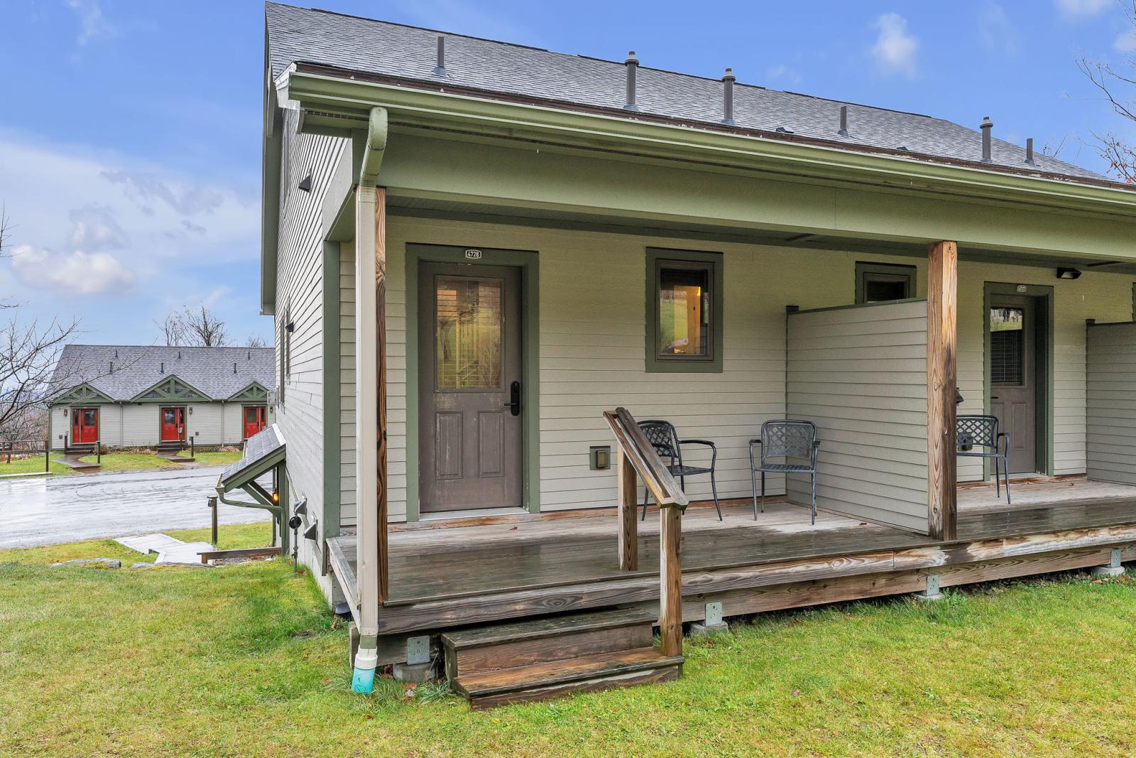 Cozy cabin with a small porch, chairs, and grassy yard under a blue sky.