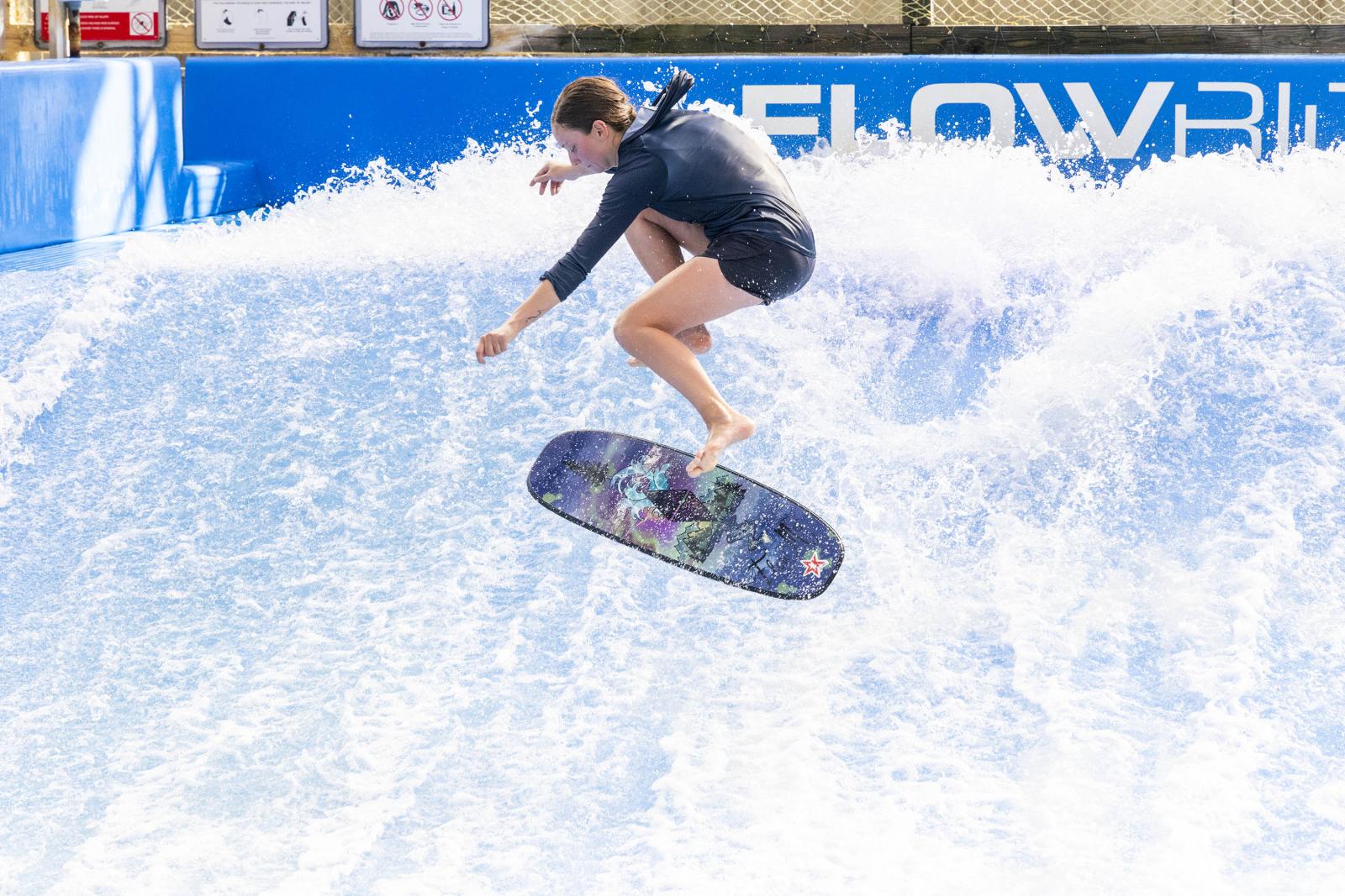 Surfer jumping on artificial wave in bright sunlight.