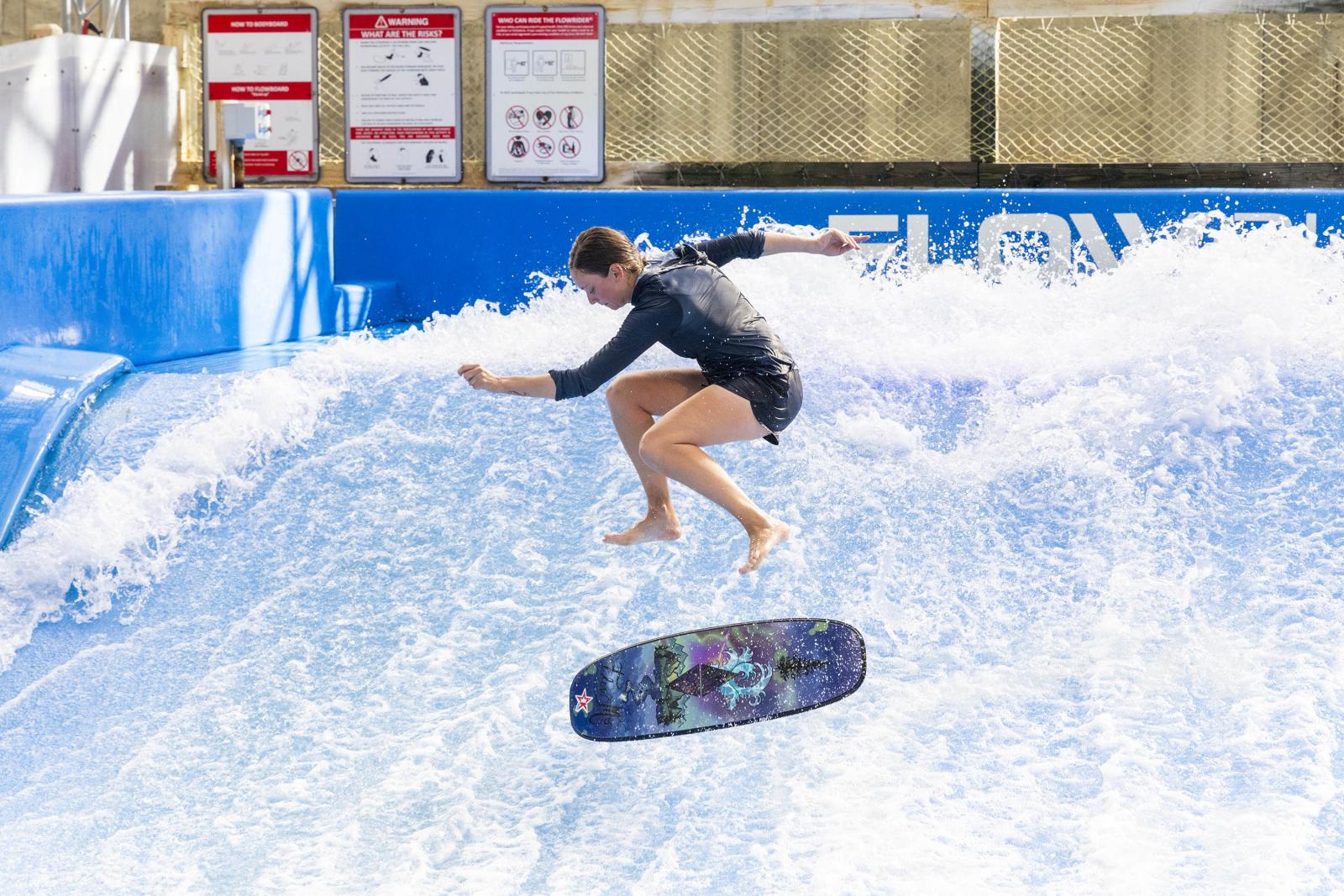 Person doing tricks on a flowrider with a surfboard in mid-air.