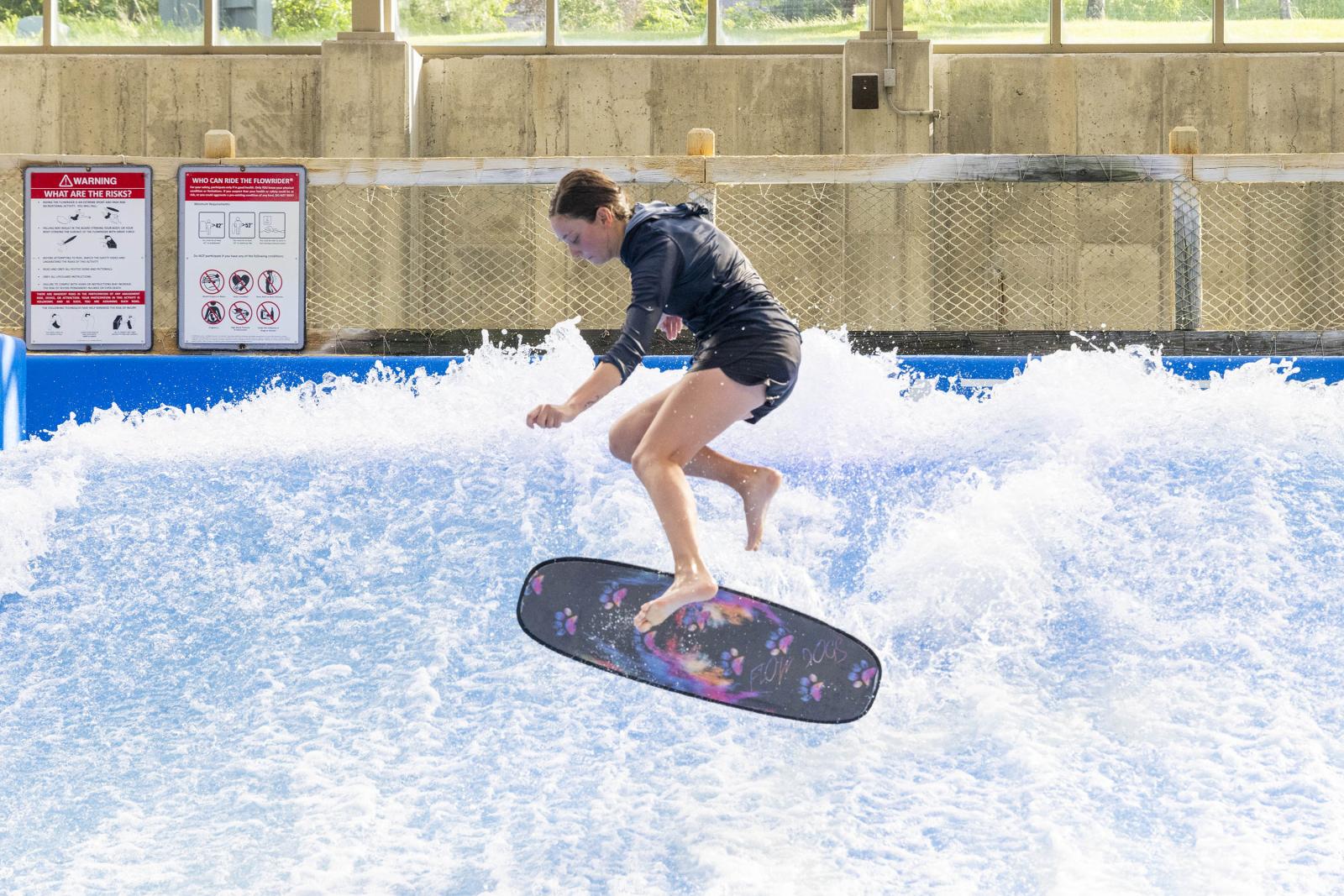 Person wear knee braces jumping on indoor wave with a bodyboard.