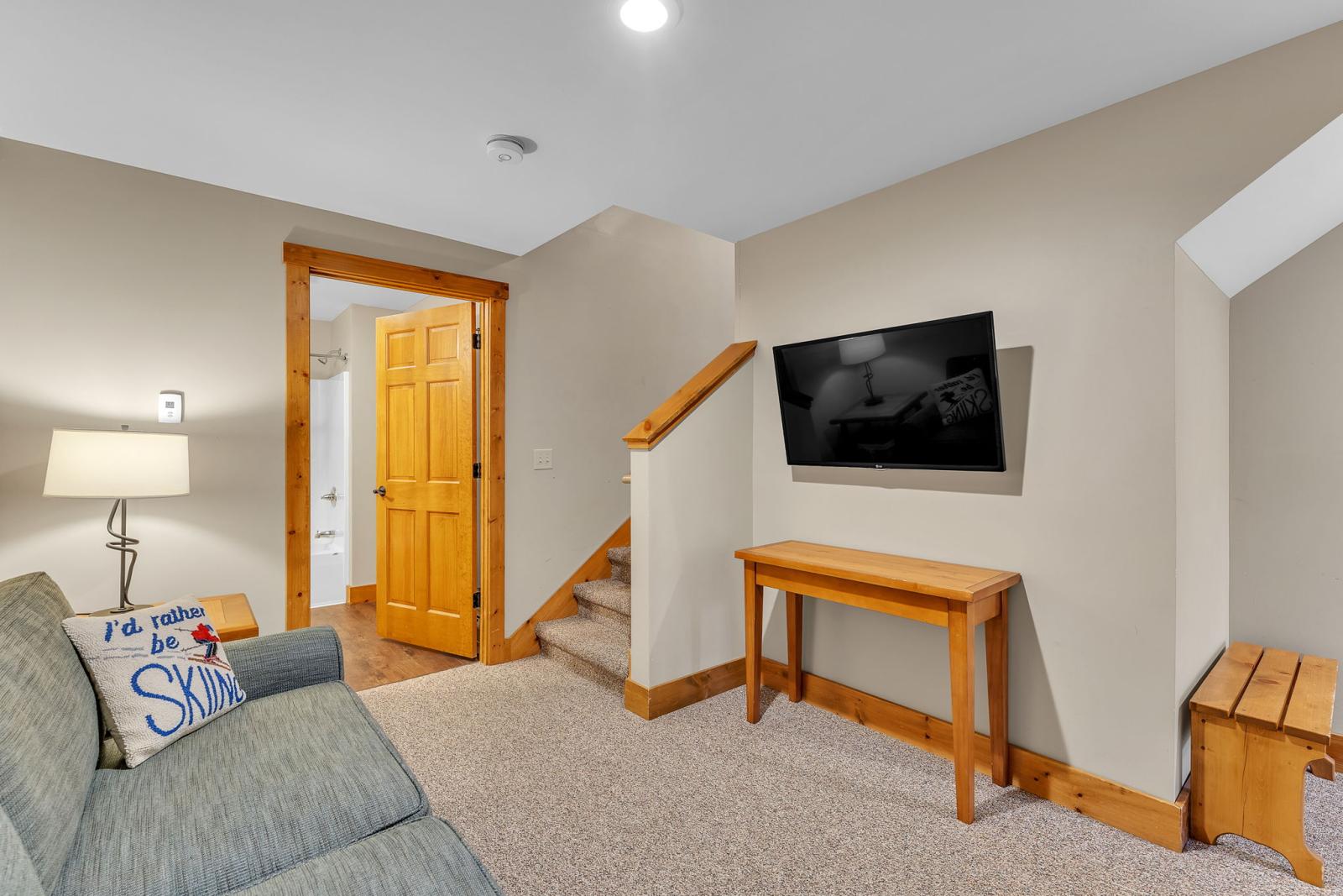 Cozy living room with sofa, lamp, TV, wooden table, and staircase.